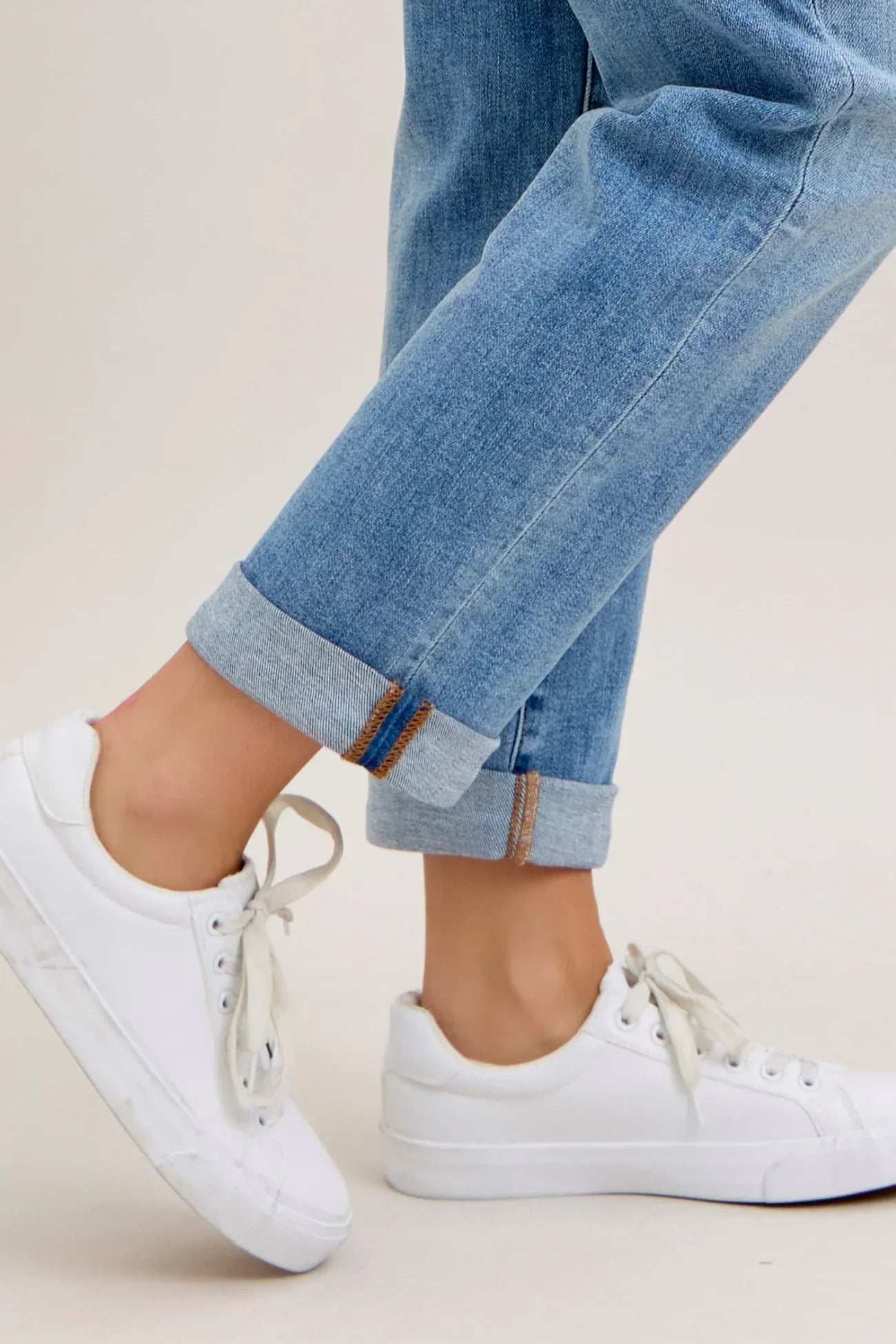 White sneakers and rolled-up blue jeans worn by a person on a light background