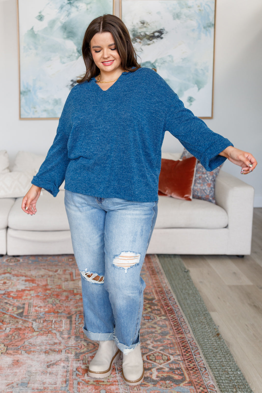 Woman wearing a blue sweater and distressed blue jeans in a living room setting