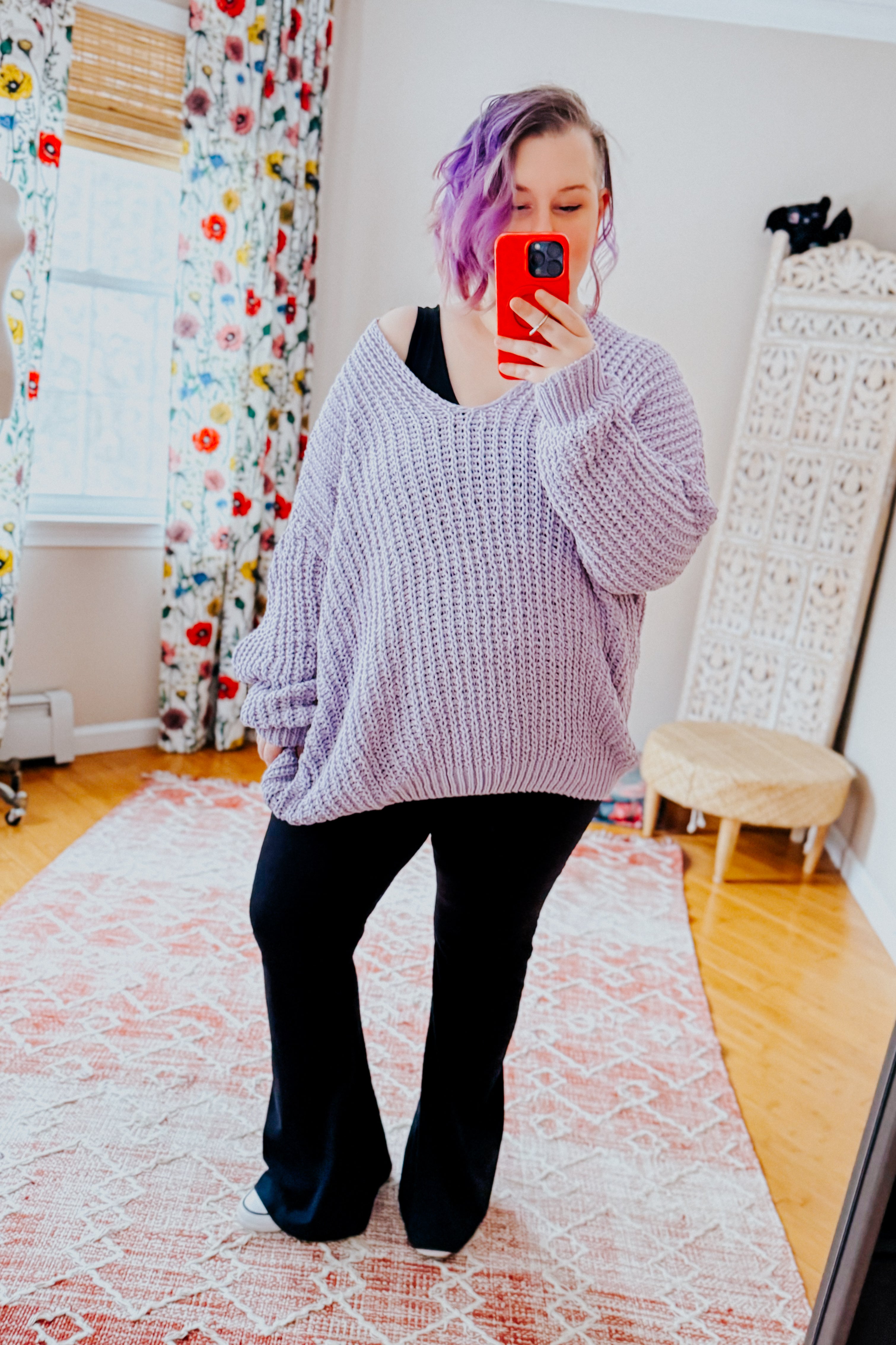 Woman wearing a chunky lavender sweater and black yoga pants in an indoor setting.
