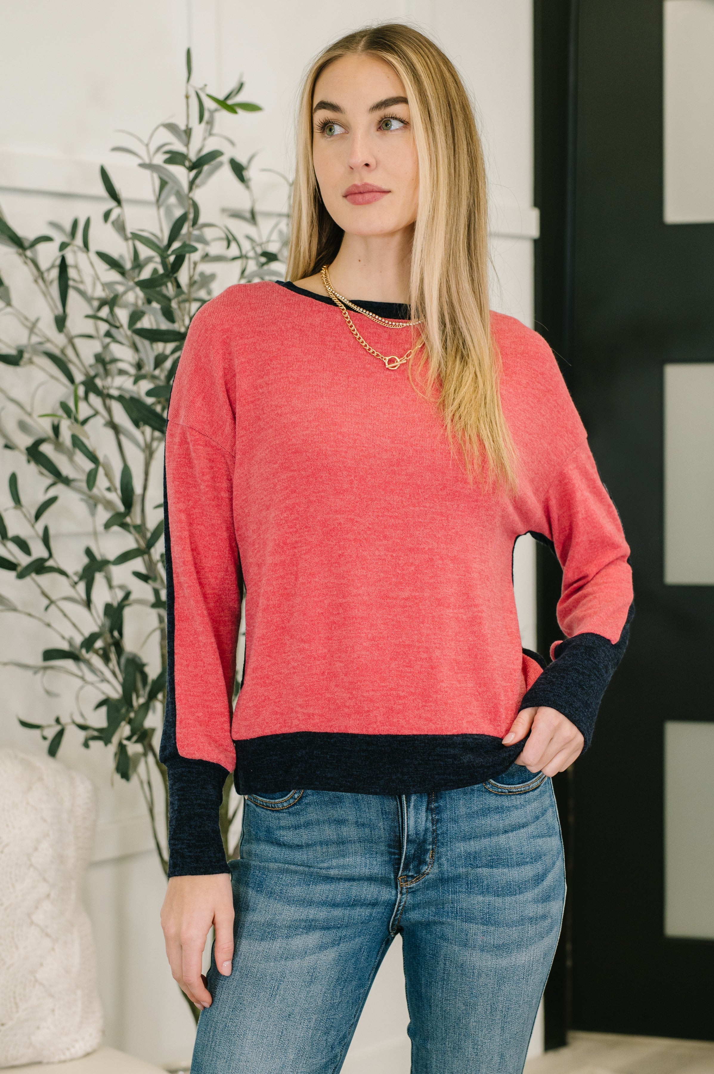 Woman wearing a red sweater with black cuffs and trim over blue jeans standing indoors.