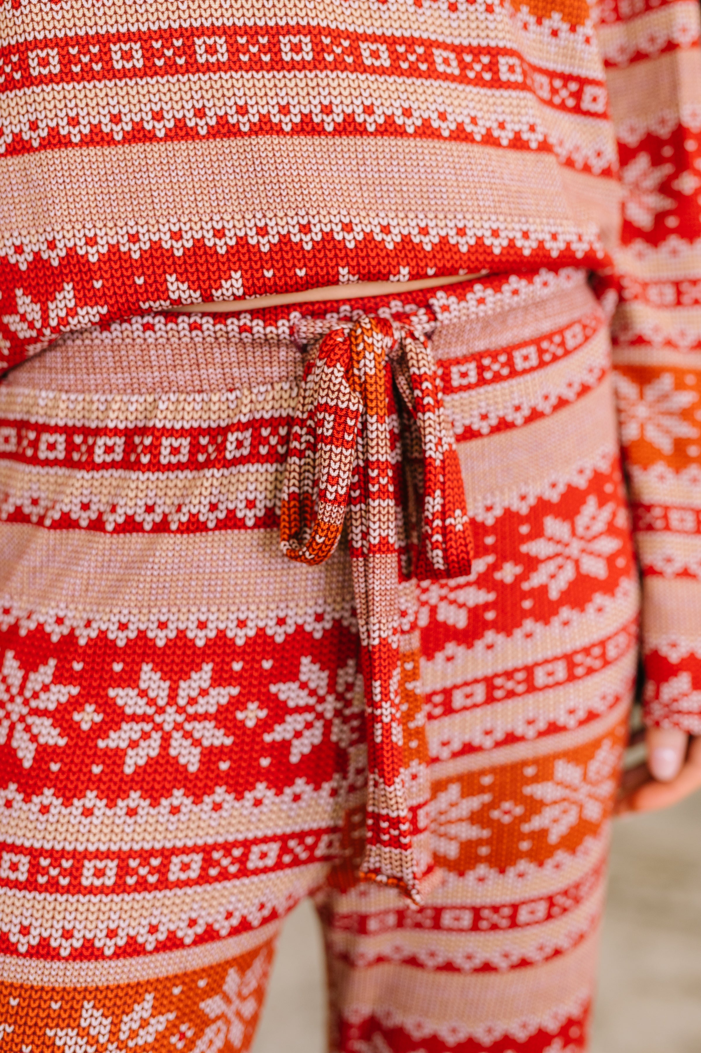 Close-up of a woman wearing a red and beige snowflake patterned pajama set with a functional tie waistband.