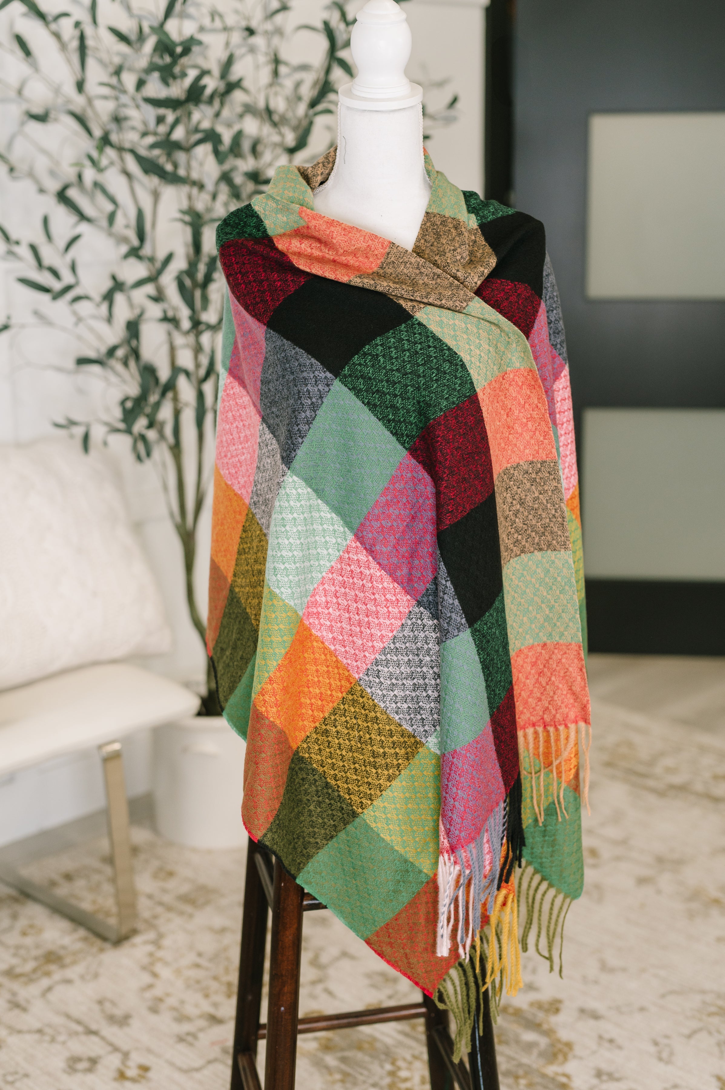 Multicolored checkered scarf with fringe draped over a dress form in an indoor setting.