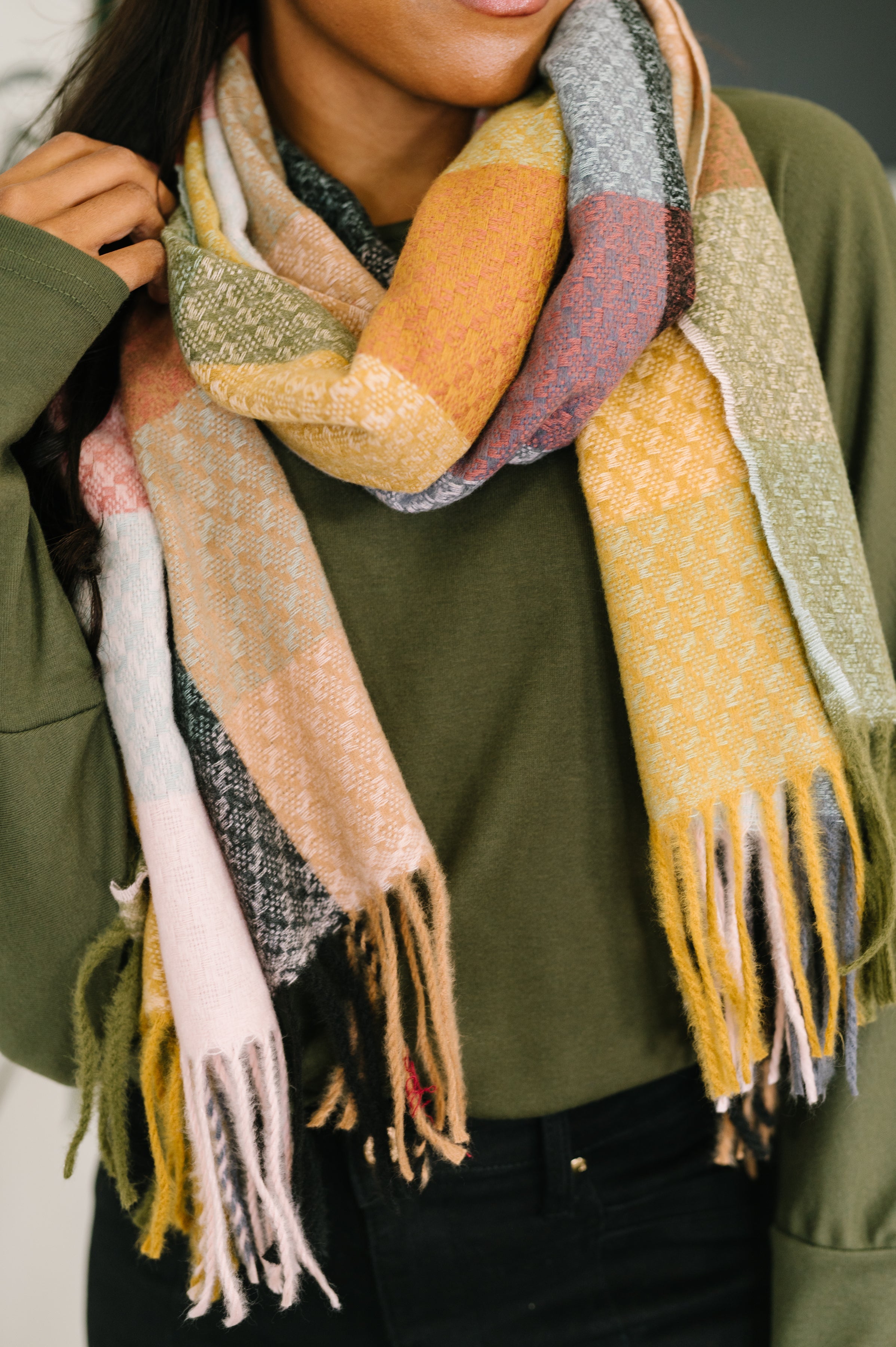Woman wearing a colorful checkered scarf with fringes on a neutral background