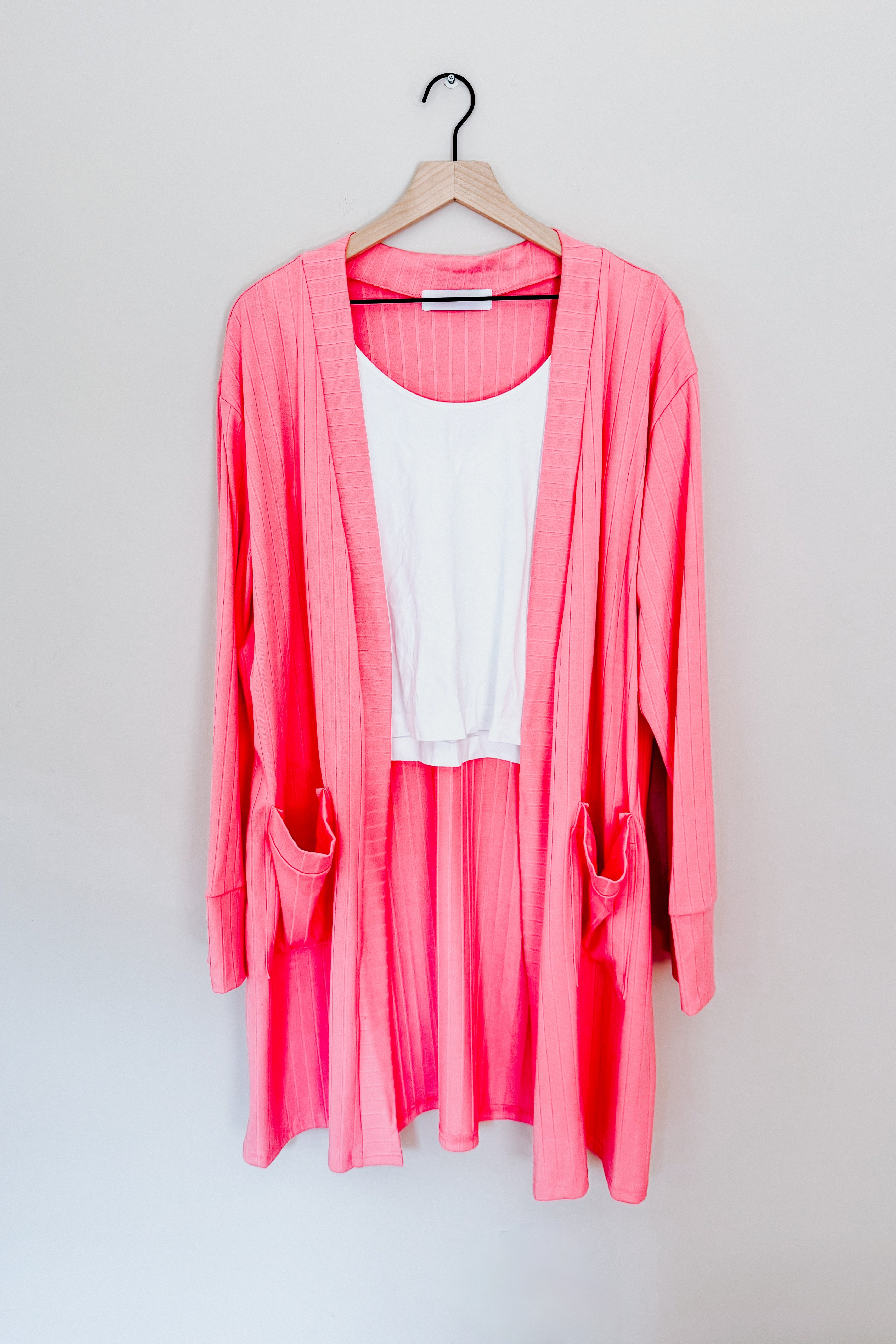 Coral ribbed Modern Idealist open front cardigan with pockets layered over white tank top on wooden hanger against wall