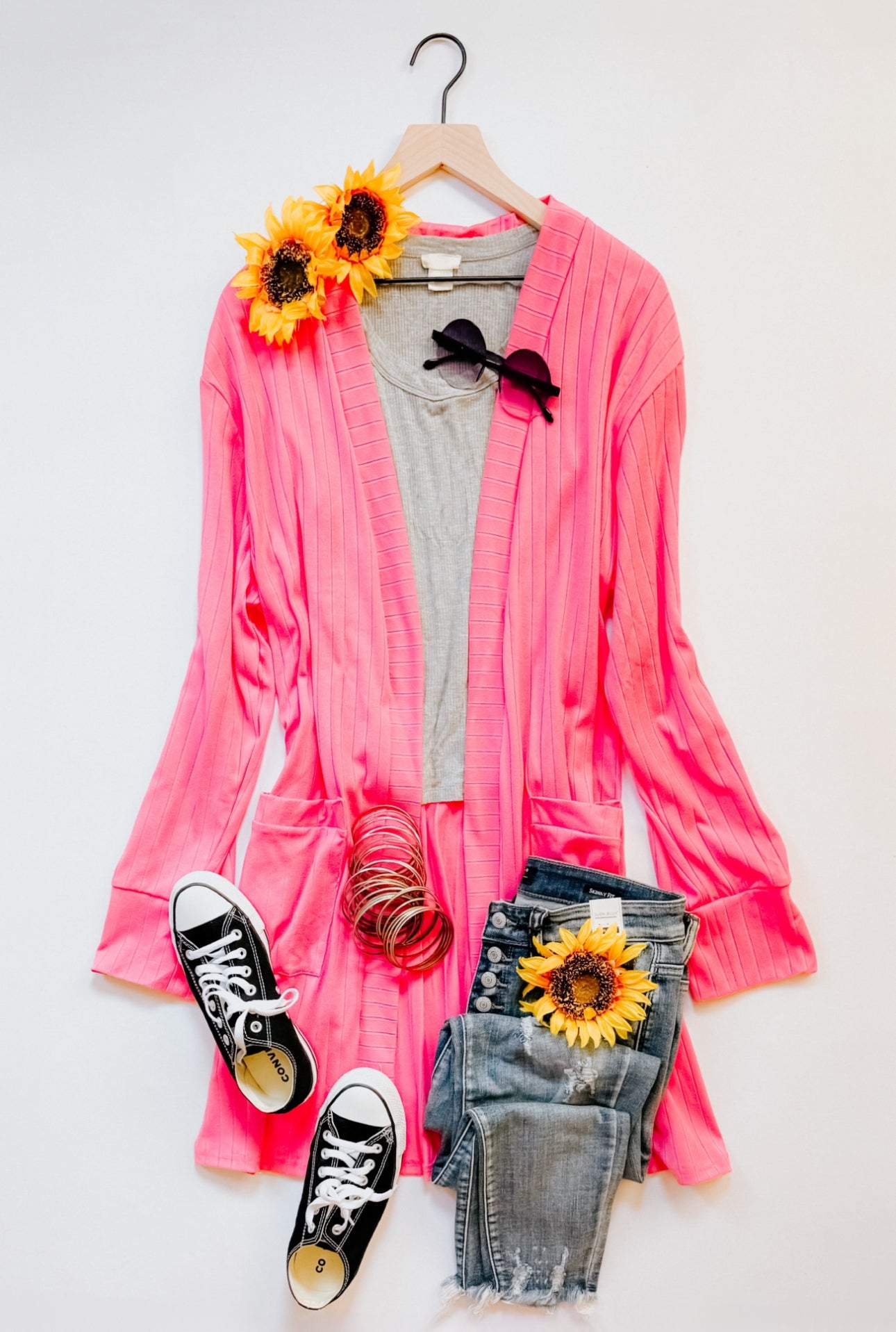 Pink ribbed Modern Idealist open front cardigan styled with gray tee, denim shorts, sneakers, sunglasses, bangles, and sunflowers on hanger