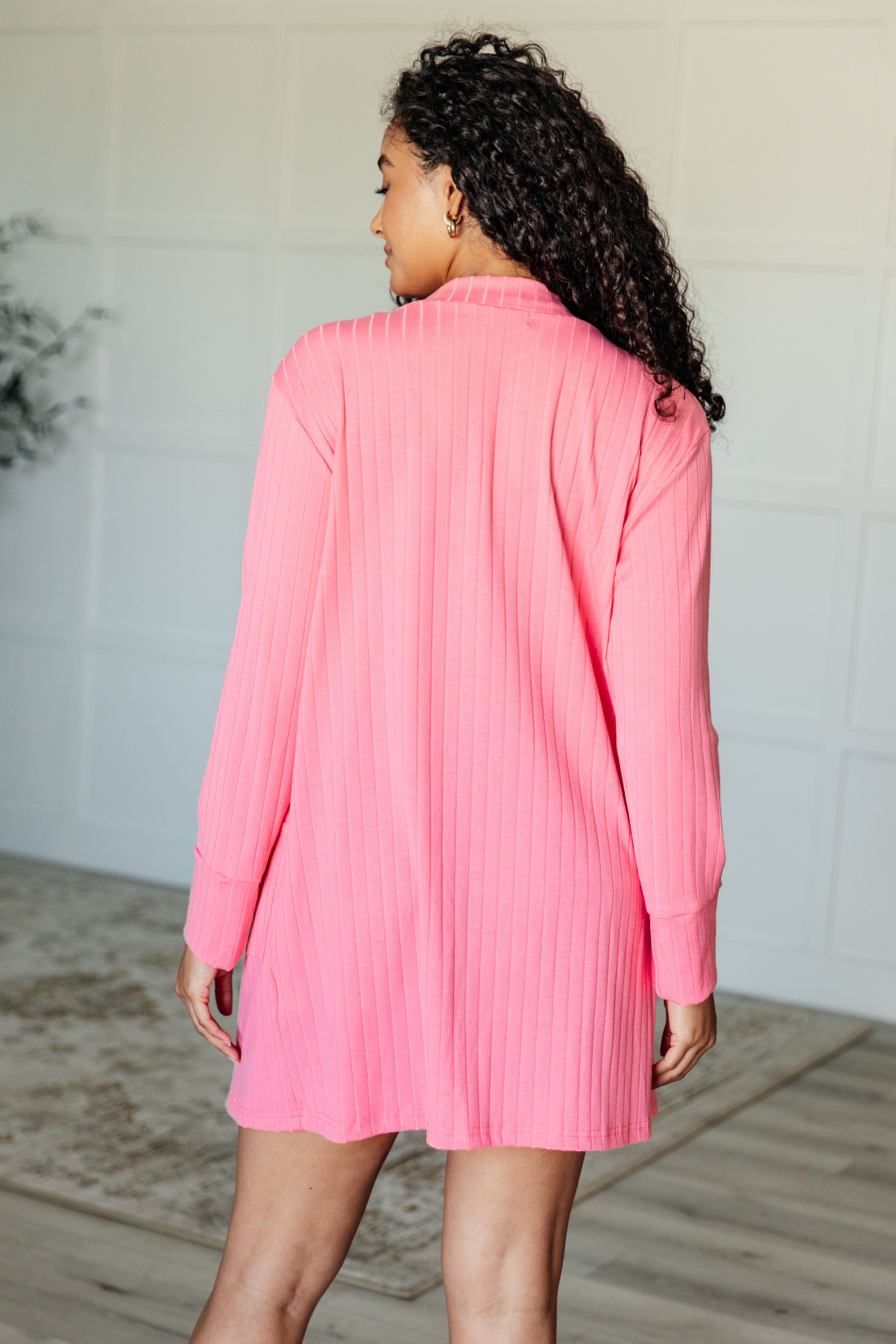 Woman seen from back wearing bright pink Modern Idealist open front cardigan with vertical ribbed texture indoors