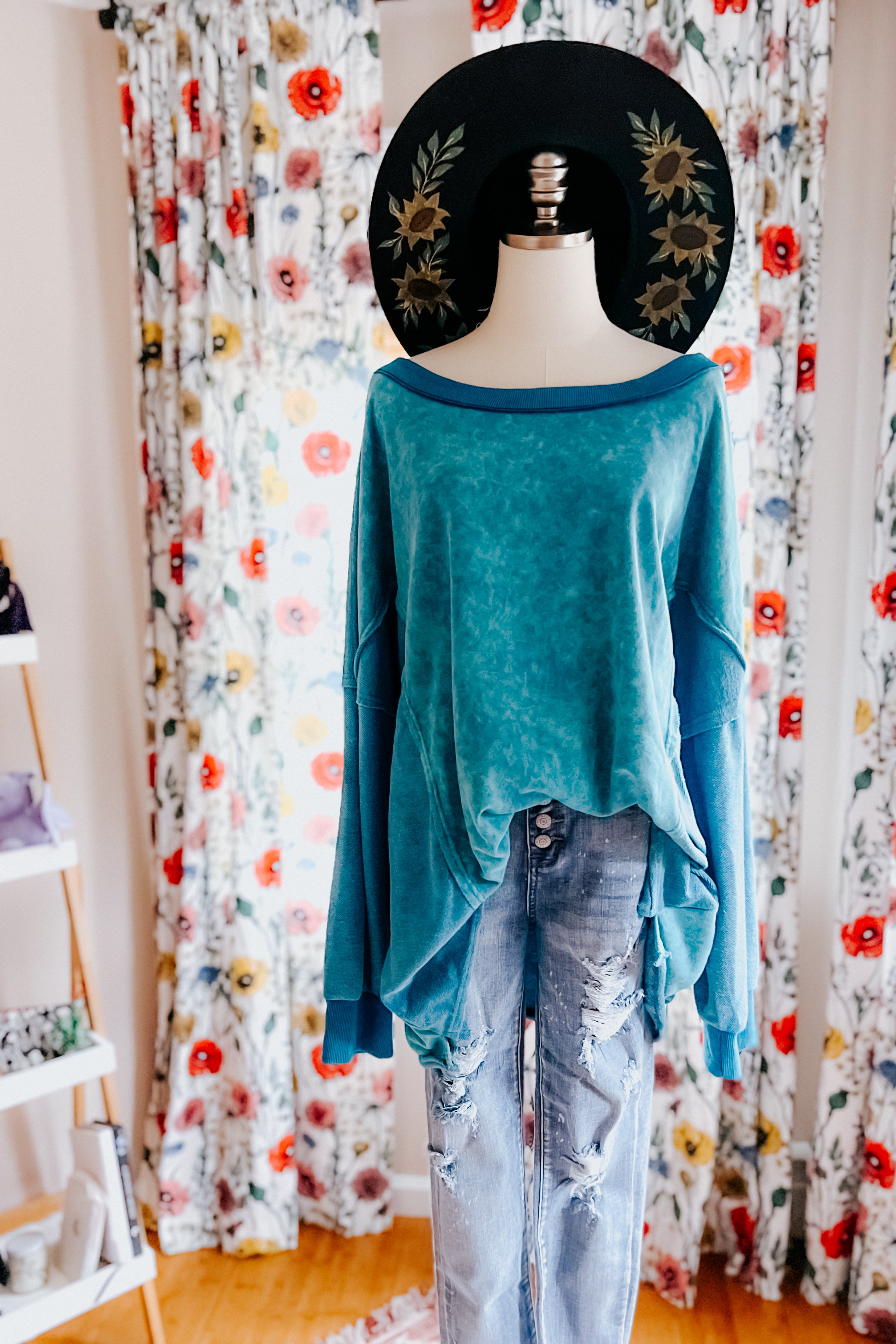 A dress form wearing a blue mineral wash pullover over blue jeans and wearing a sunflower hat against an indoor setting.