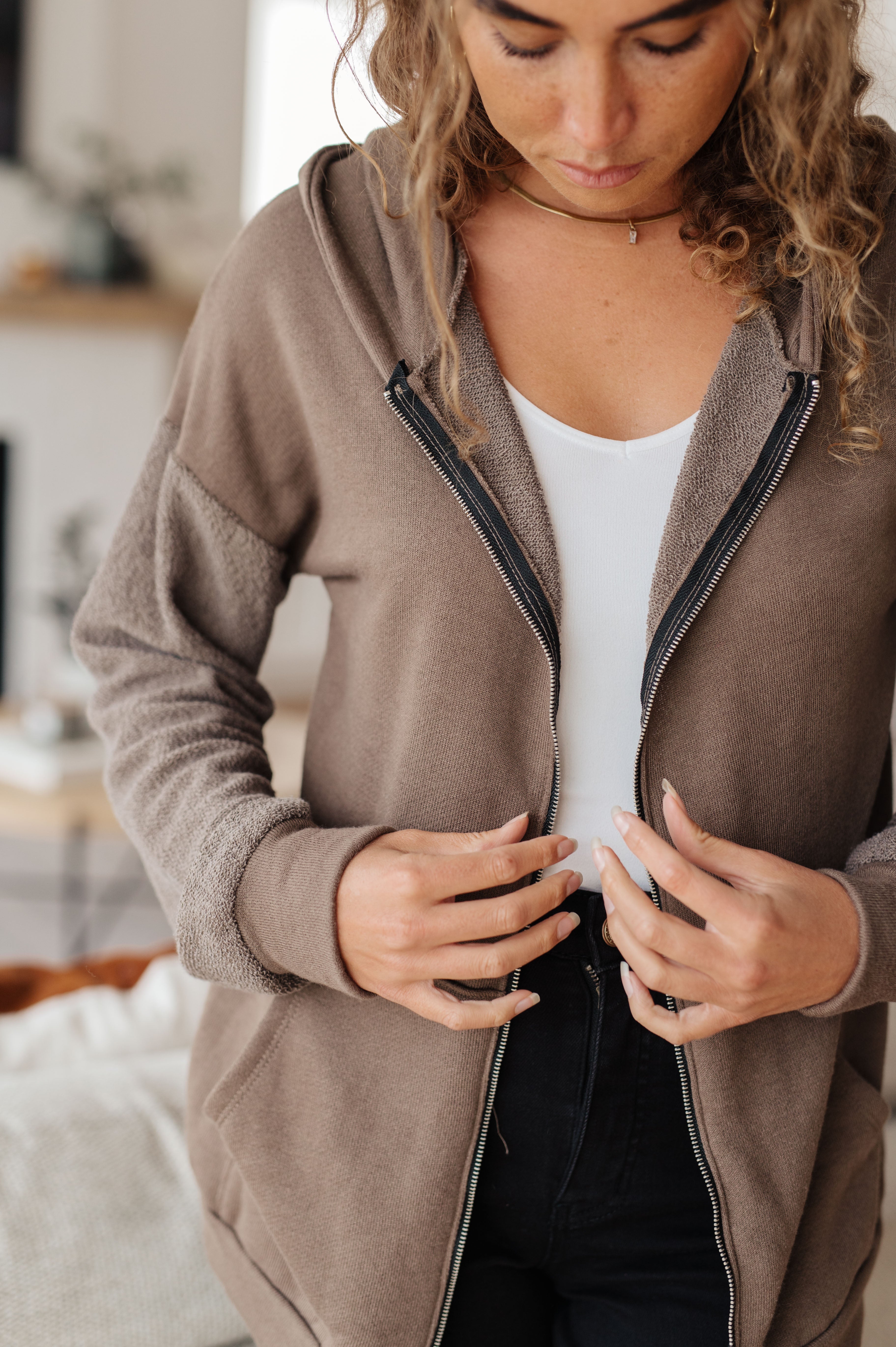 Woman with her back facing the camera wearing a brown zip-up hoodie over over black jeans in a casual indoor setting.