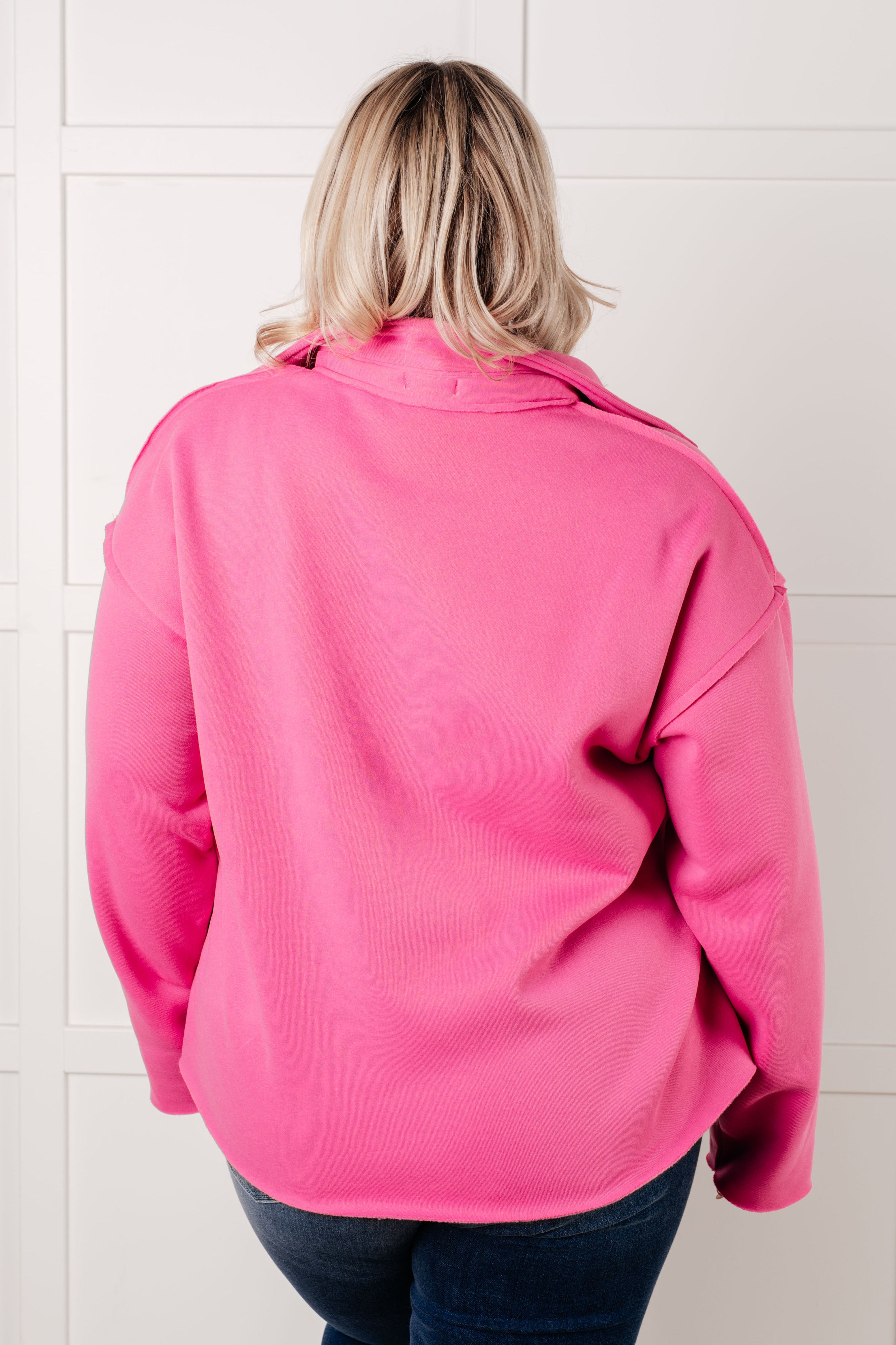 Woman wearing a hot pink colored pullover with exposed seams and blue jeans with a white background.