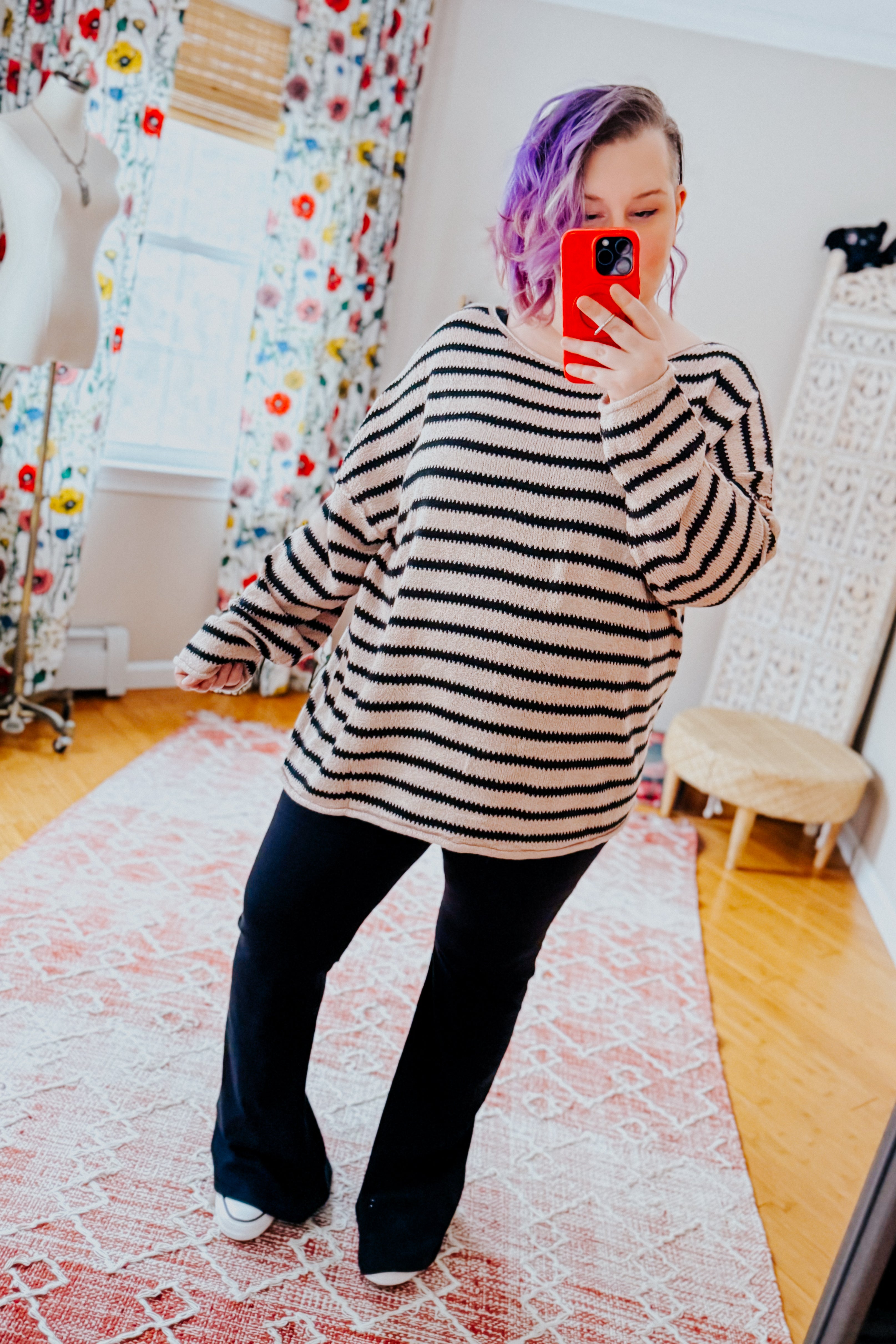 Woman wearing a taupe long sleeve sweater with black stripes and yoga pants in an indoor setting.