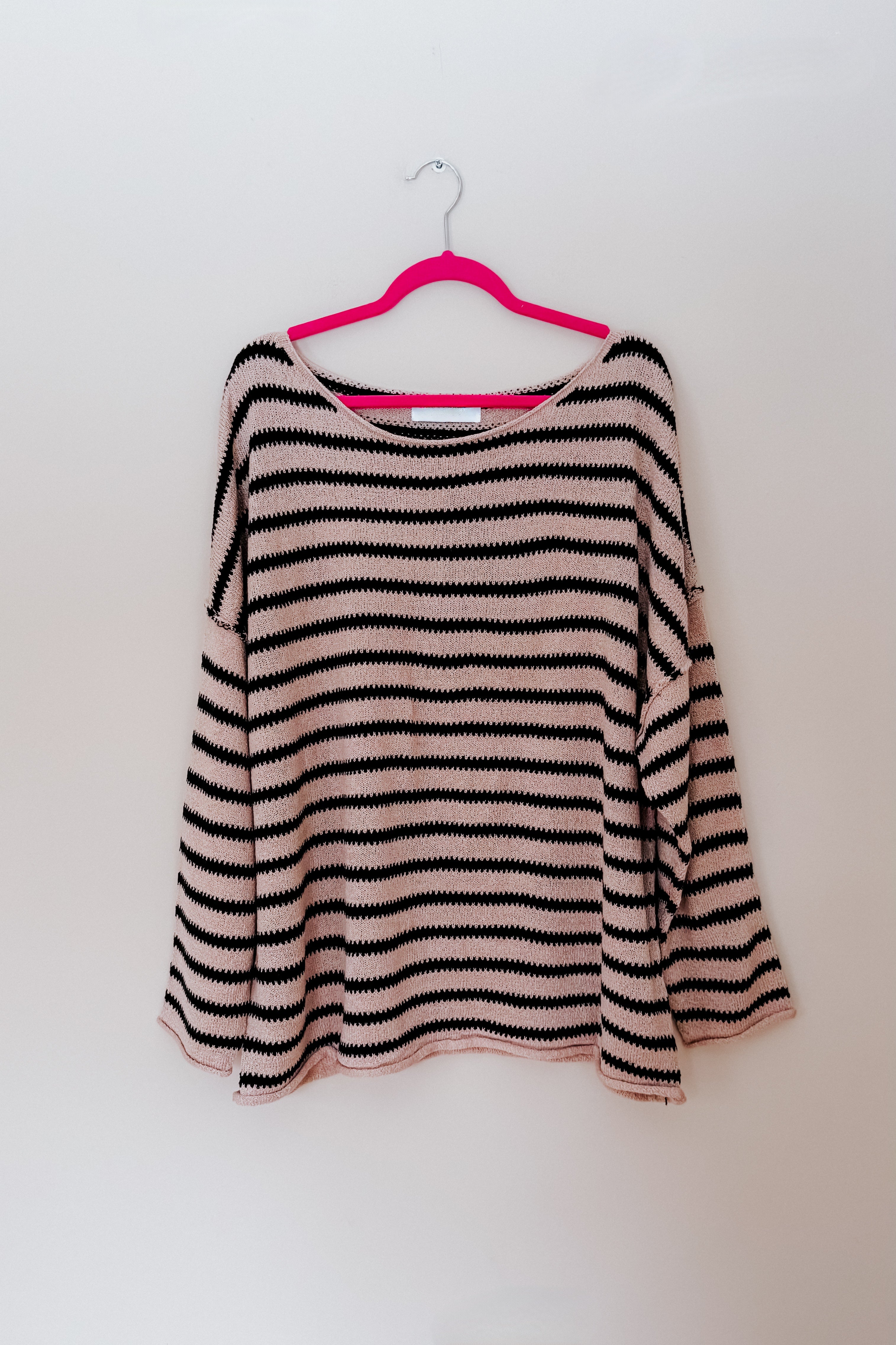 A taupe long sleeve top and black stripes hanging on a pink hanger.