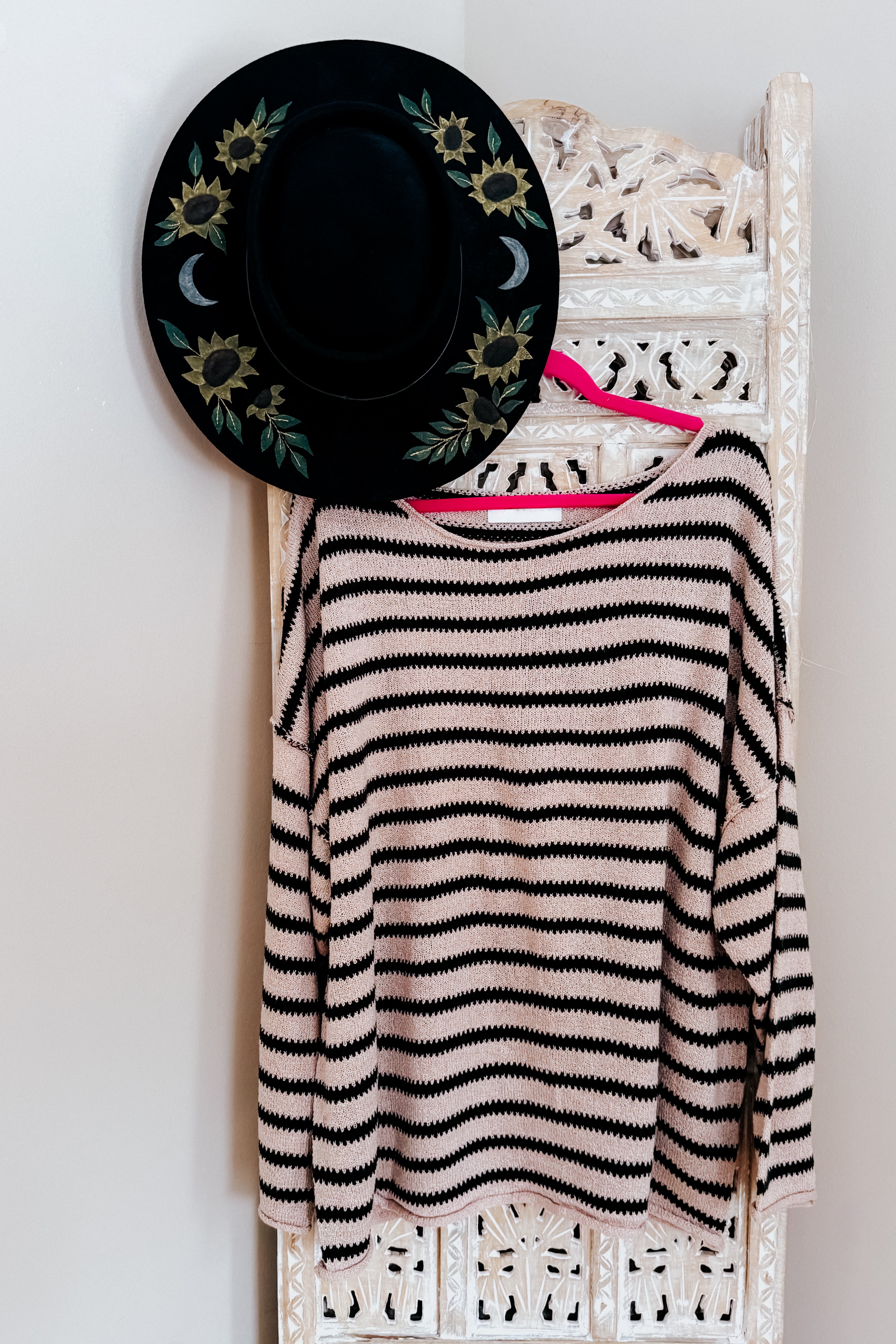 A taupe long sleeve sweater with black stripes hanging on a rustic room divider with a painted wide brim hat.