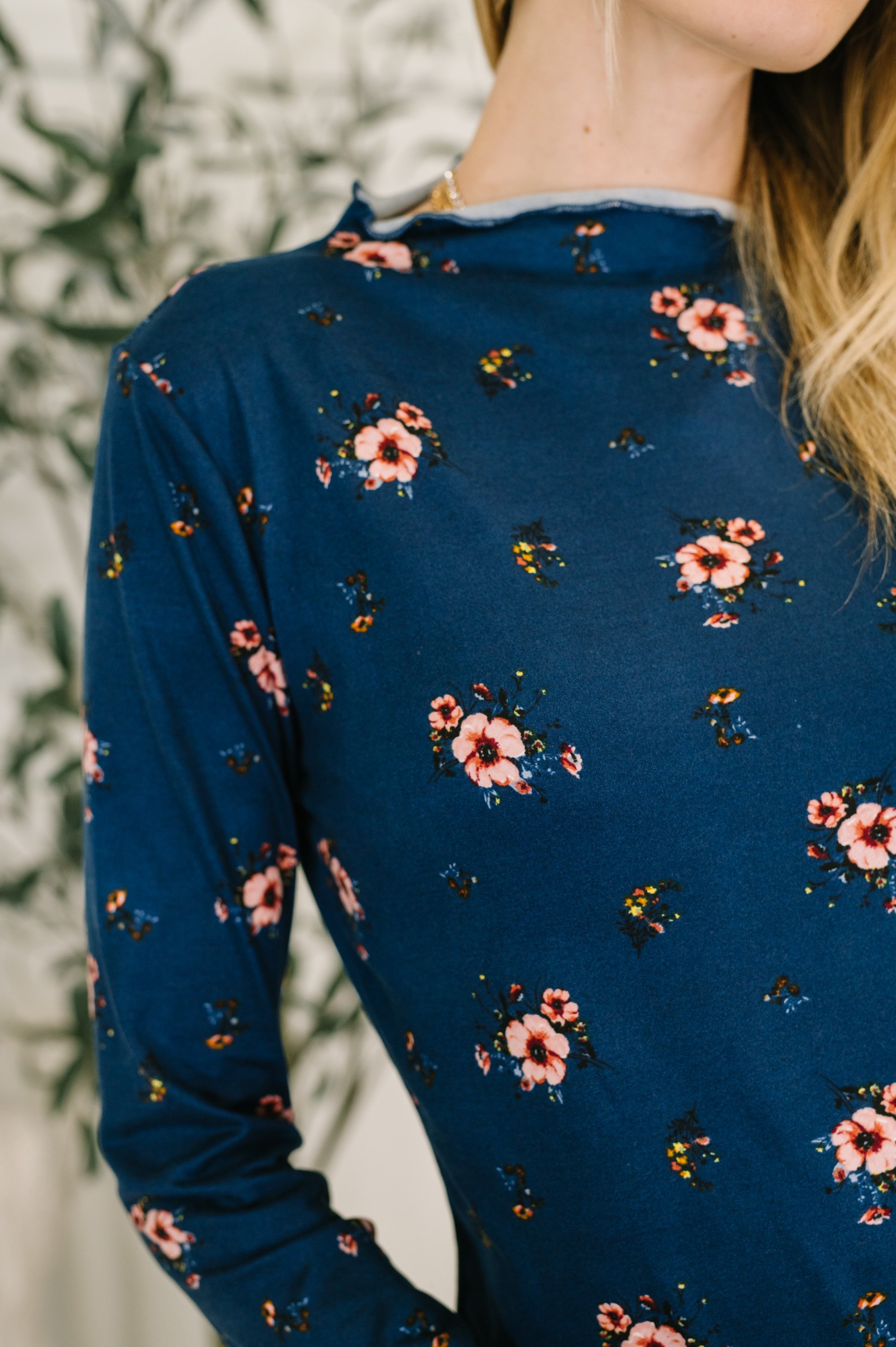 Close up of a woman wearing a blue long-sleeve floral print shirt against a blurred background.