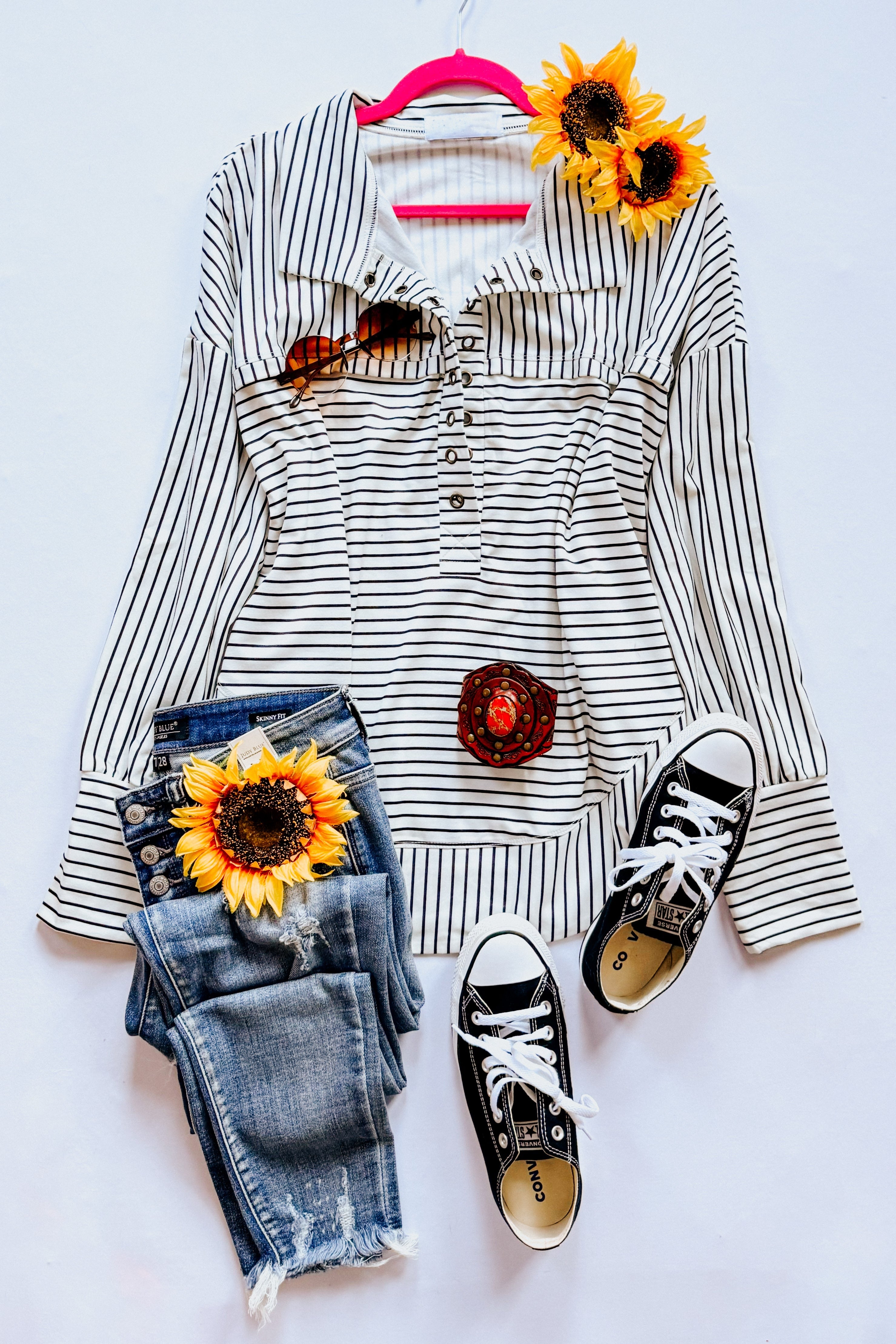 A flat lay display showing a white and black striped collared pullover top, blue jeans, black converse sneakers, accessories and decorative accents.