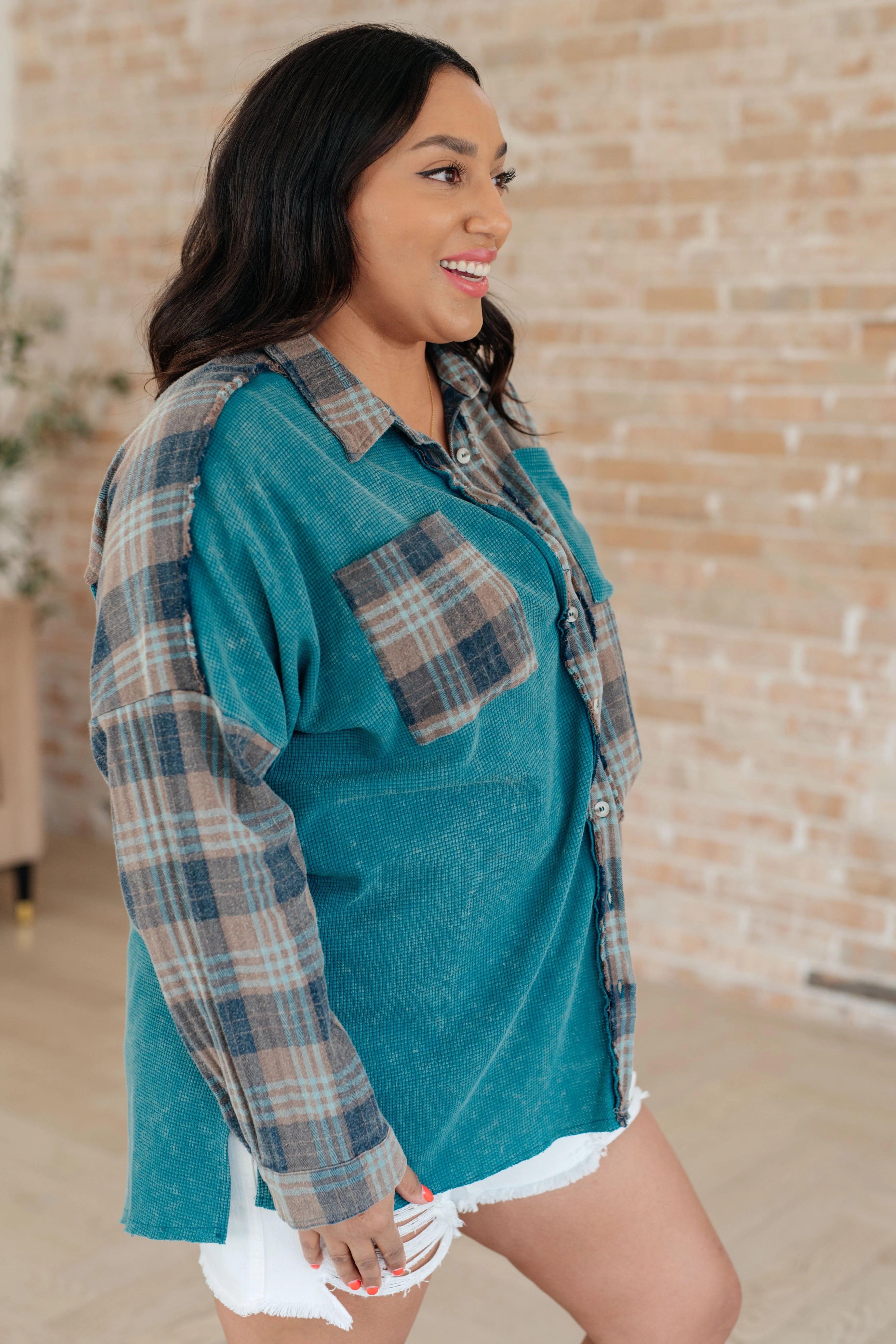 Woman wearing a blue plaid button up shirt over white distressed shorts with a brick wall background