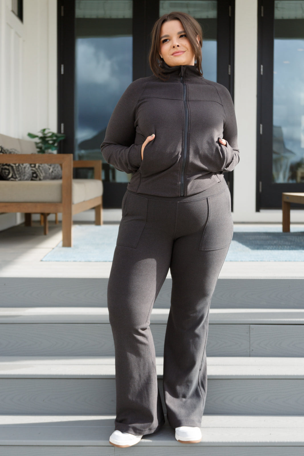 Woman in a grey zip-up jacket and pants standing on steps outside a house.