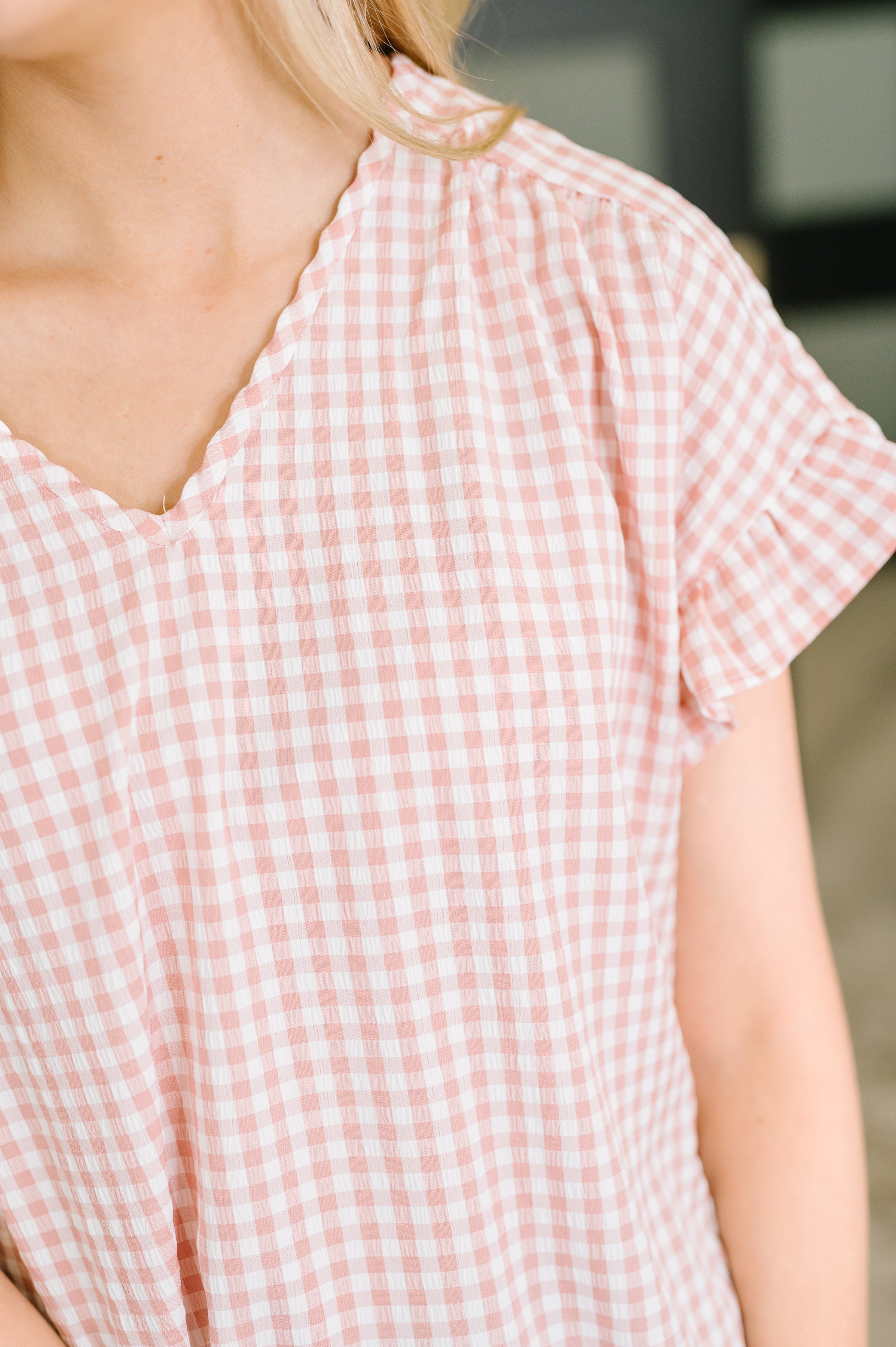 Close up of woman wearing a dusty rose gingham blouse with a V neckline and ruffle sleeves