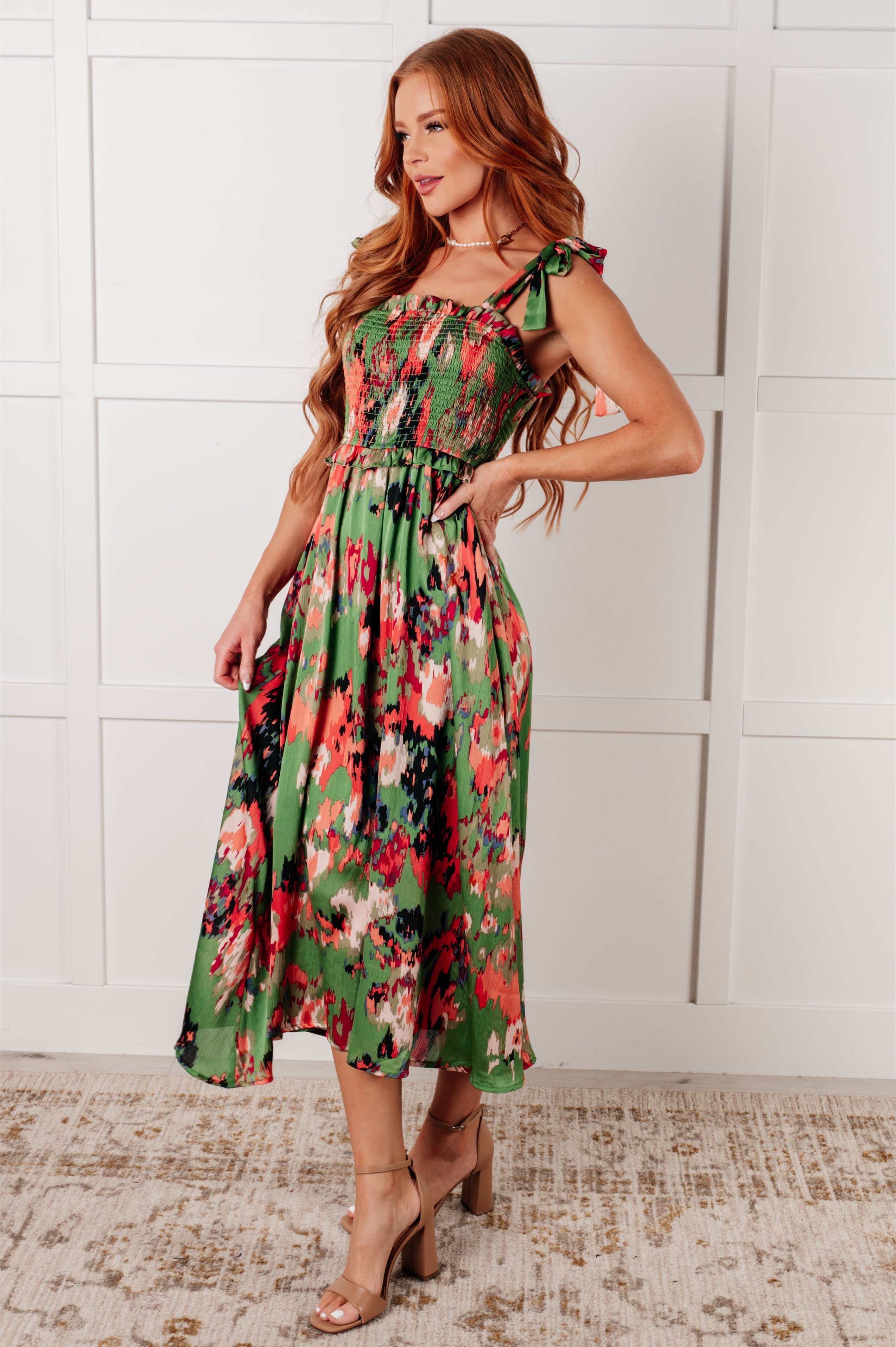 Woman wearing green floral smocked midi dress with tie shoulder straps and flowing skirt, standing indoors side view