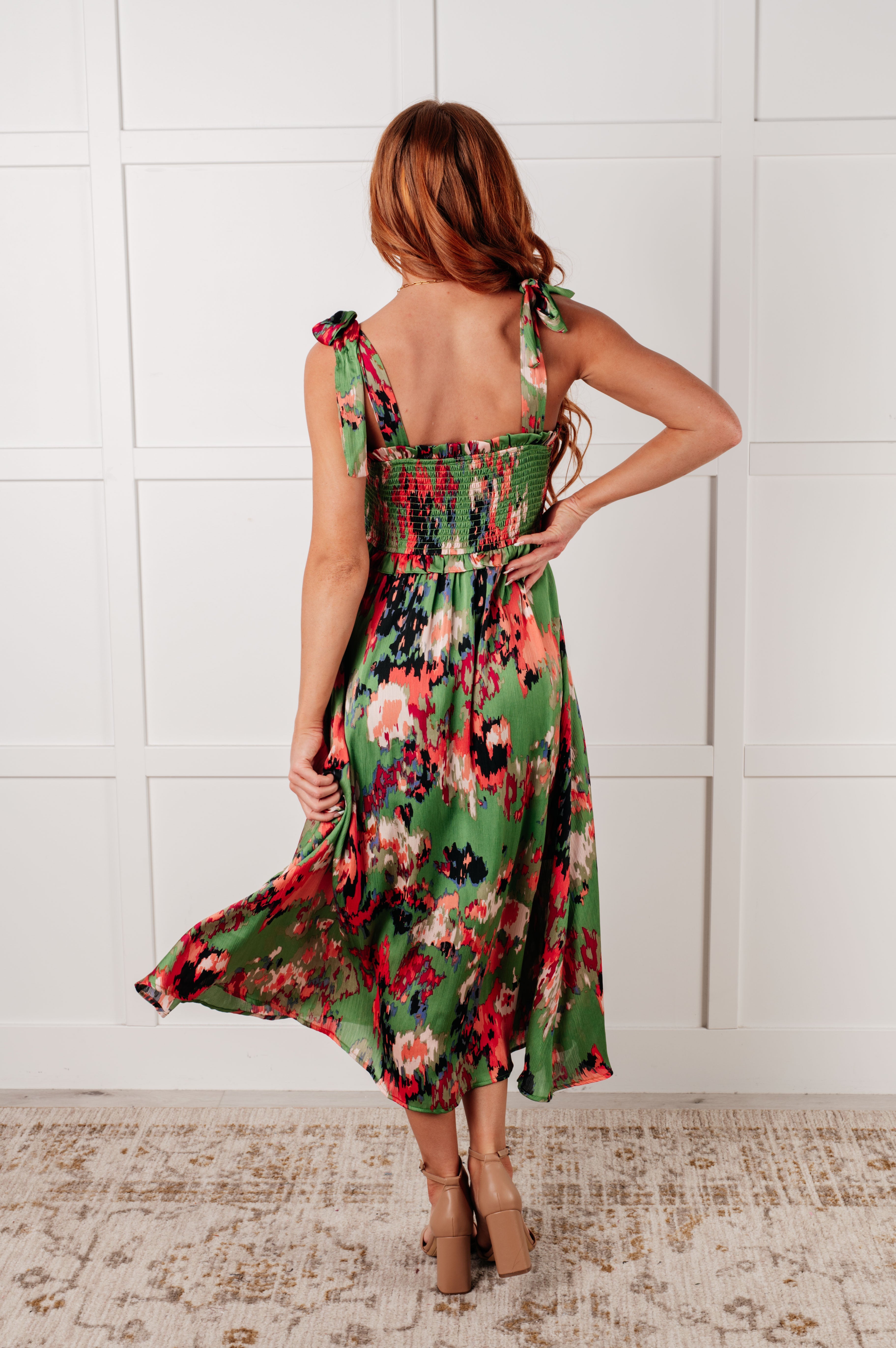 Woman seen from back wearing green floral tie-strap dress with smocked bodice and flowing skirt indoors