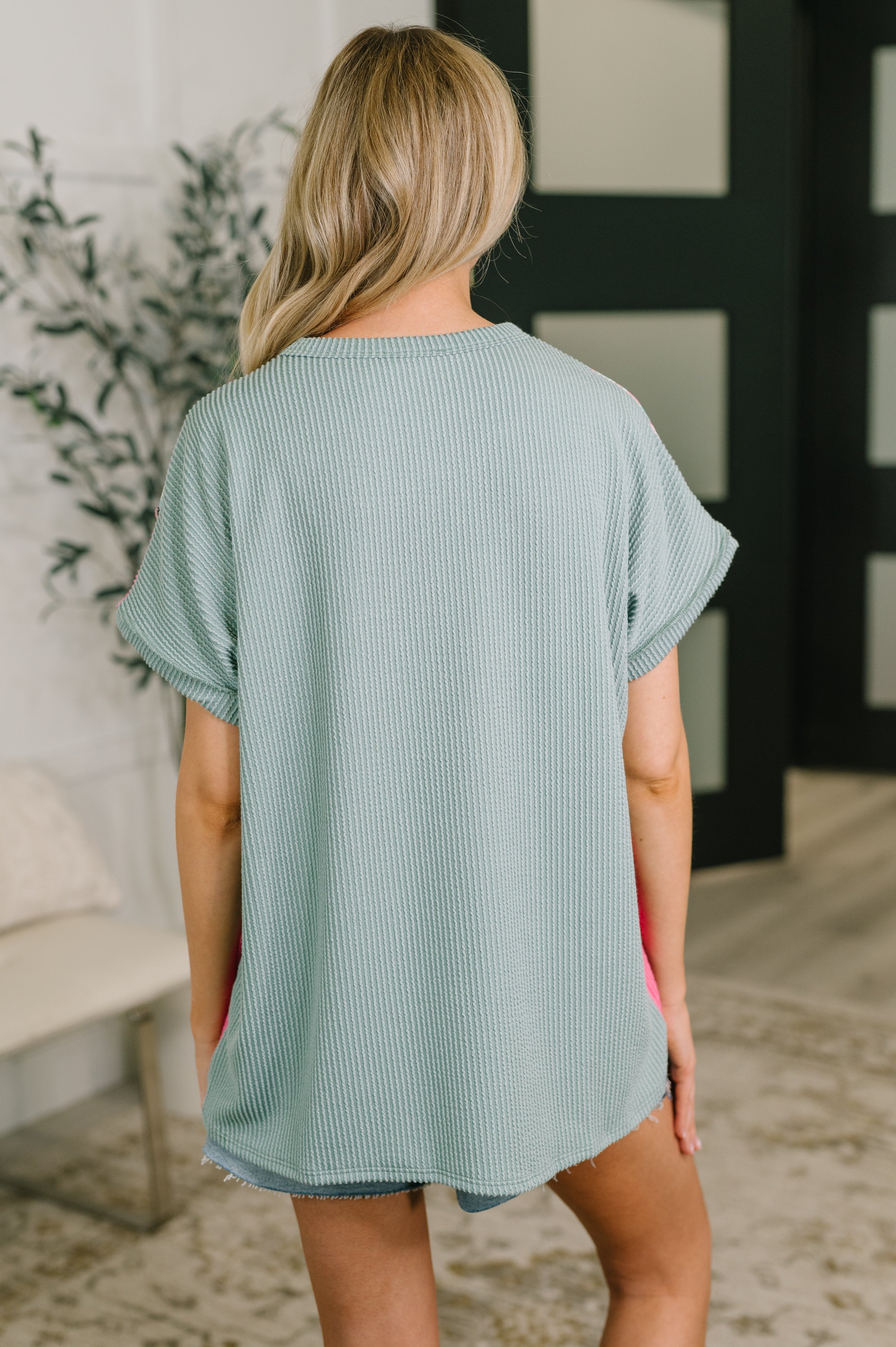 Back view of woman wearing textured blue colorblock top with rolled sleeves in a cozy indoor setting