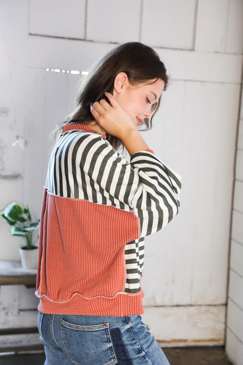 Side profile of woman wearing a crew neck pullover with black and white stripes and rust textured back panel indoors