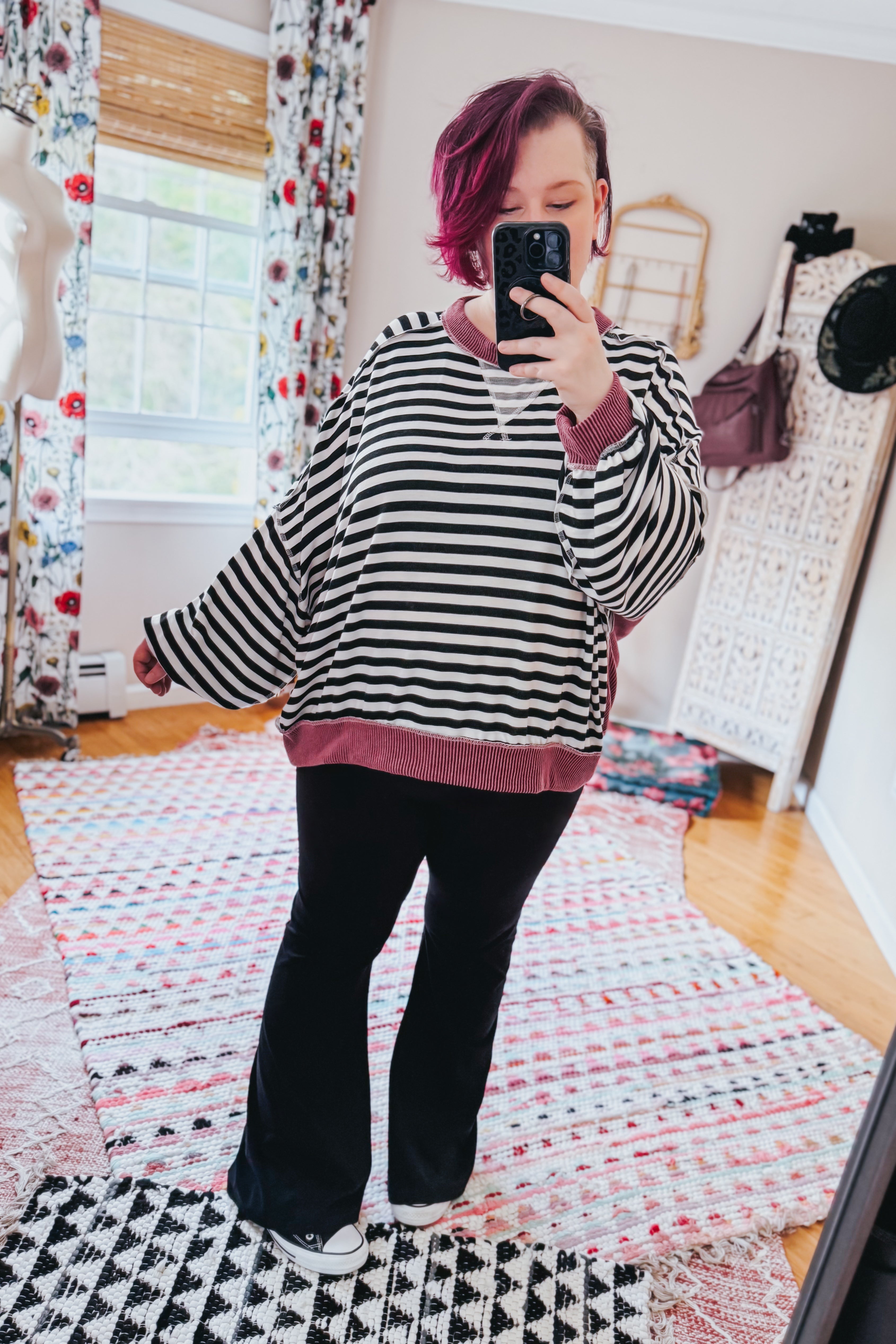Woman with short magenta hair wearing oversized black and white striped pullover with wine ribbed trim taking mirror selfie indoors