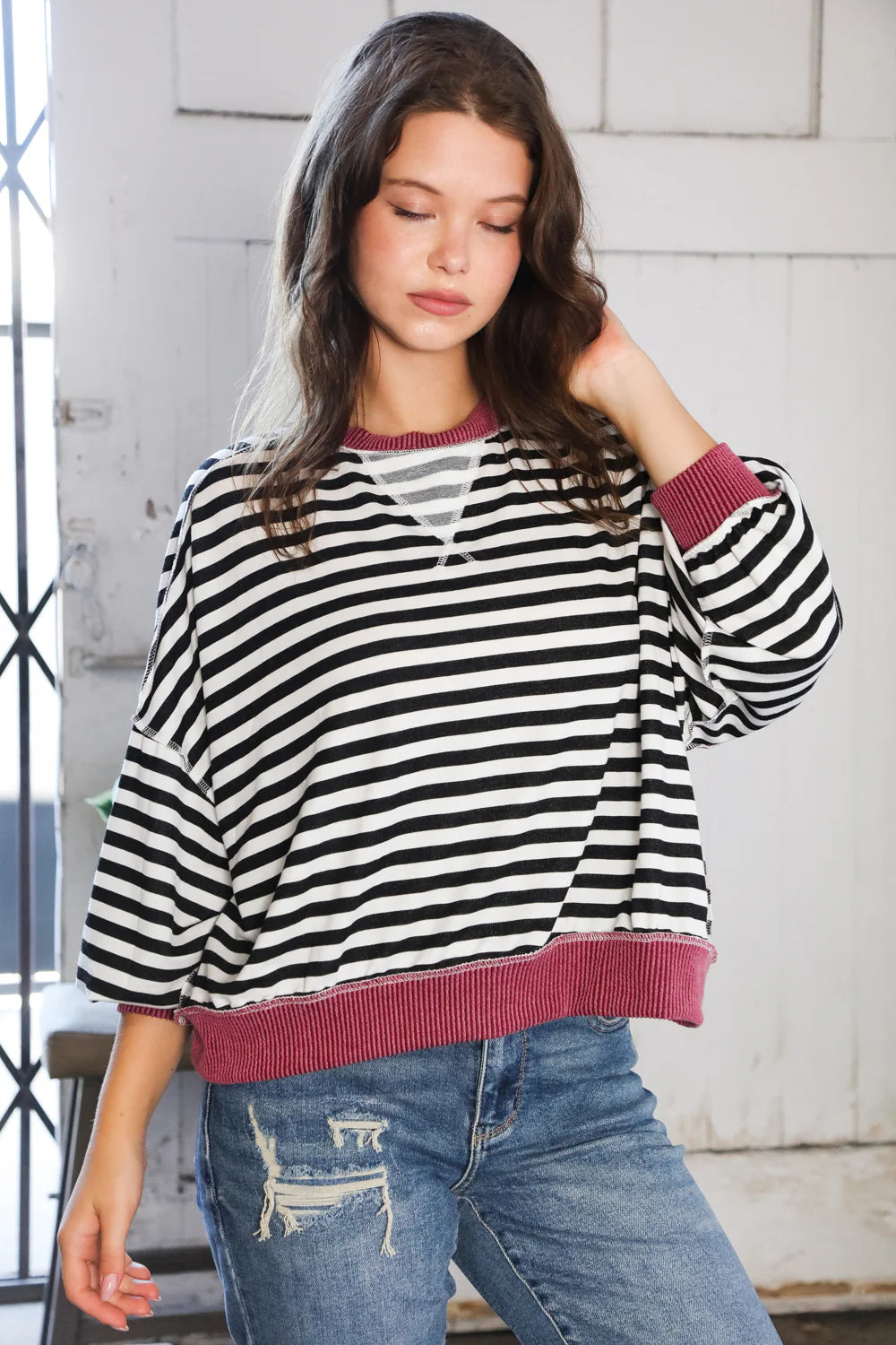 Woman wearing loose black and white striped crew neck pullover with wine ribbed cuffs and hem posing indoors near door