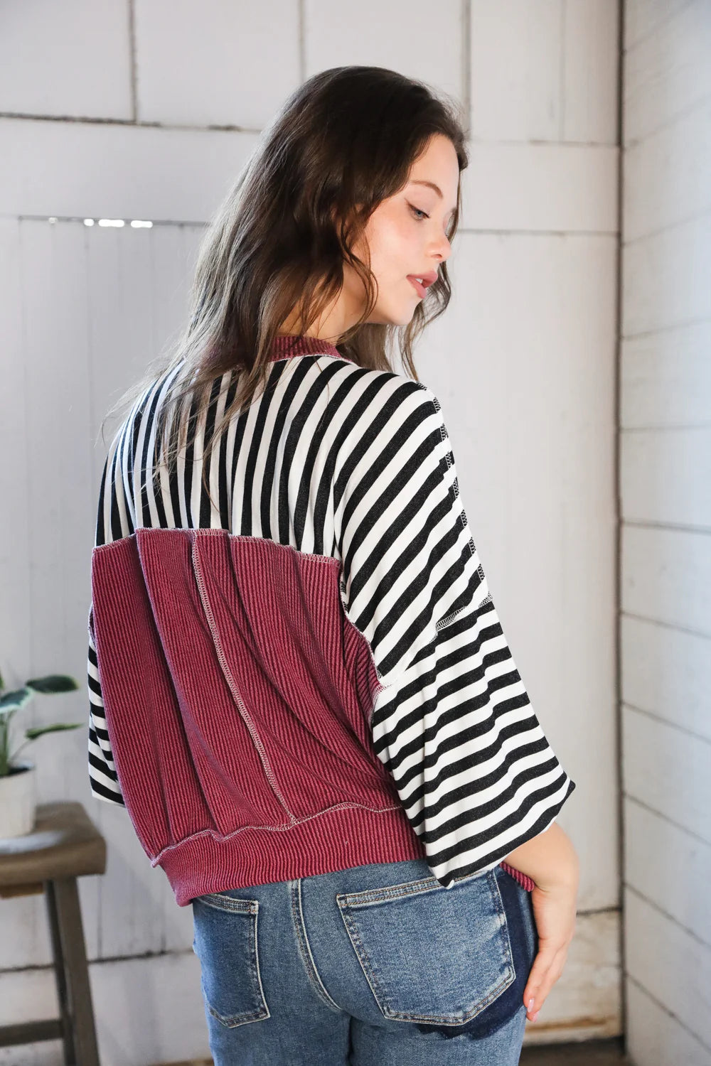 Woman showing back of striped crew neck pullover with wide sleeves and wine ribbed textured back panel indoors