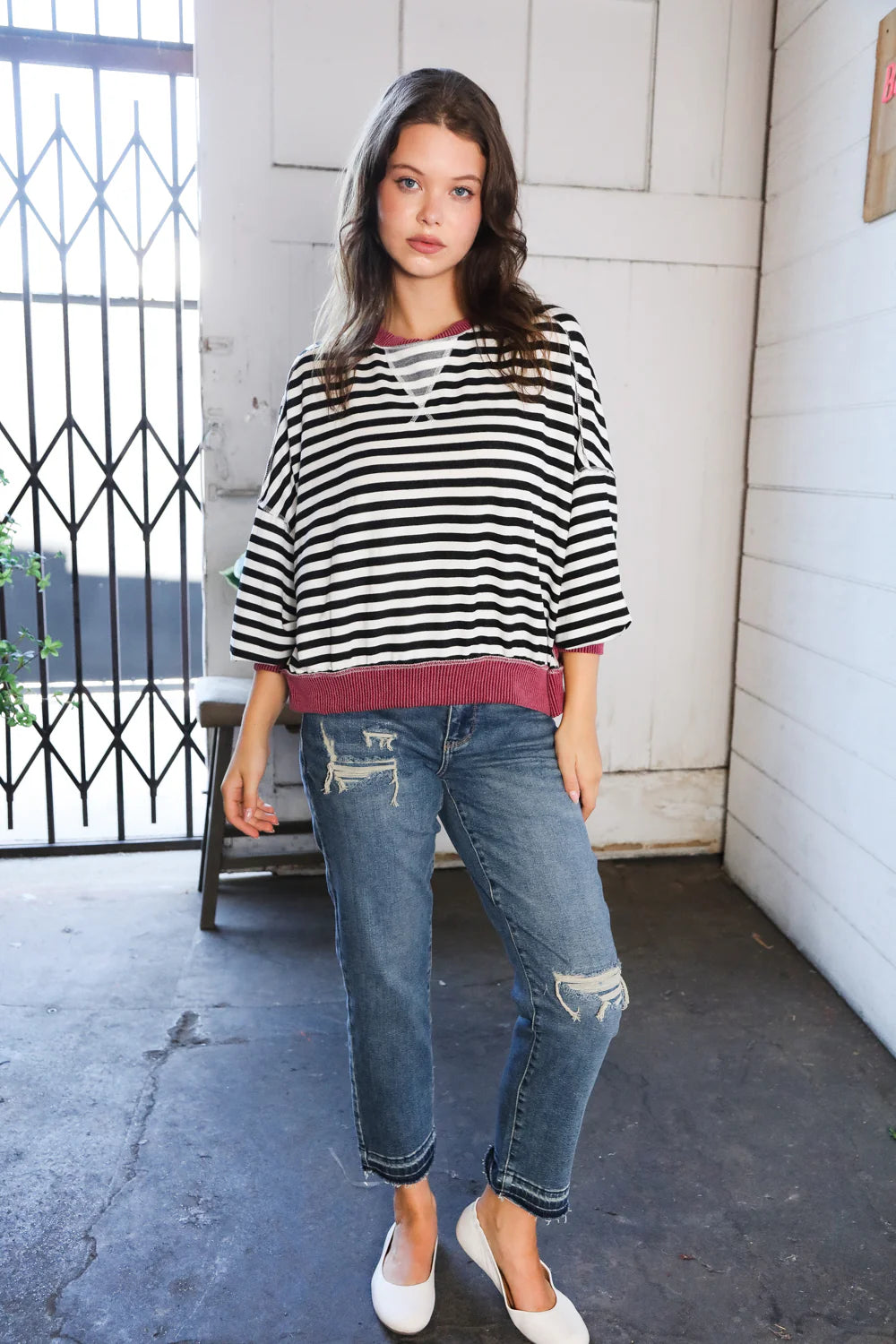 Young woman in relaxed striped crew neck pullover with wine ribbed hem and distressed jeans indoors near gate
