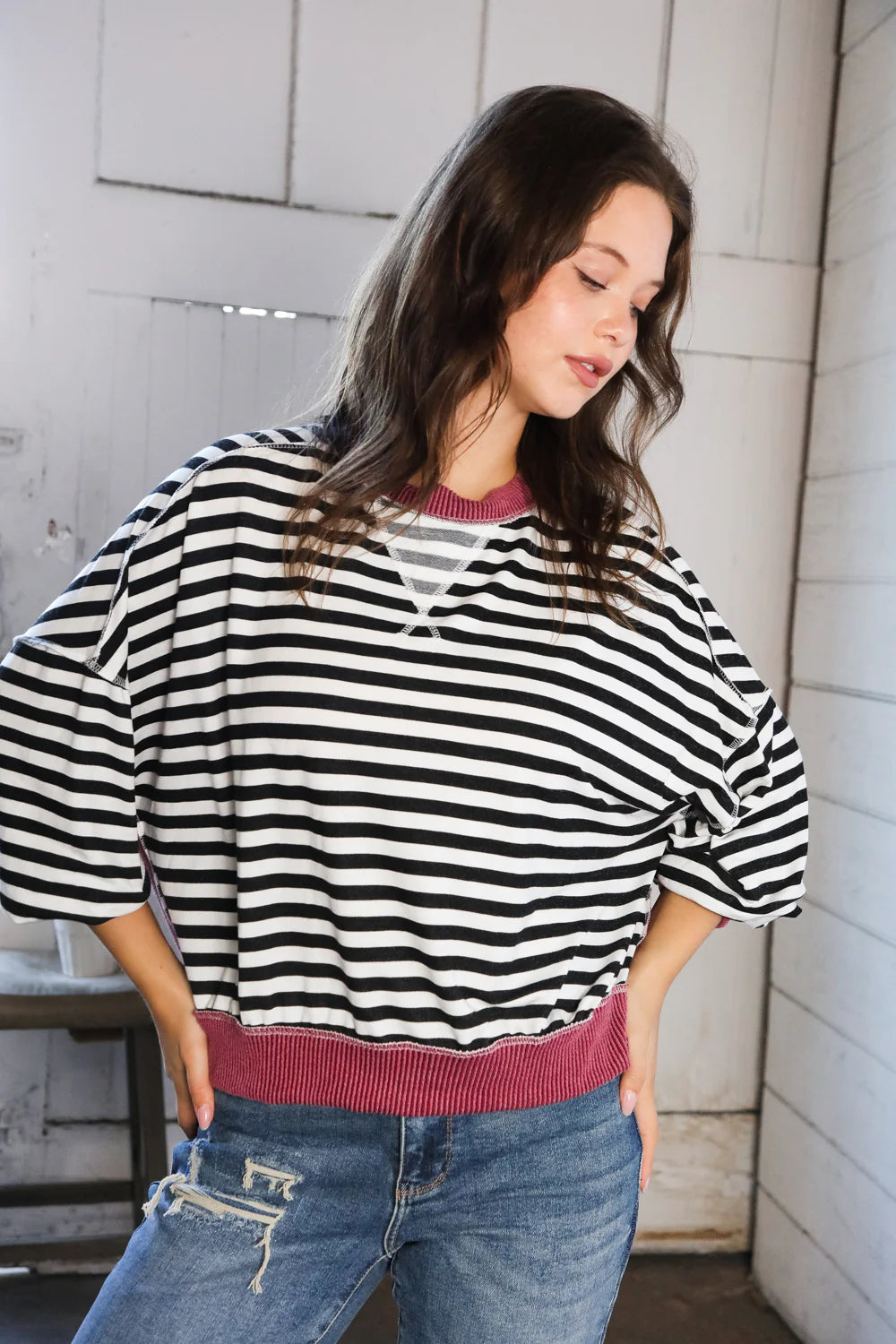 Woman wearing oversized black and white striped crew neck pullover with wine ribbed trim and distressed jeans indoors