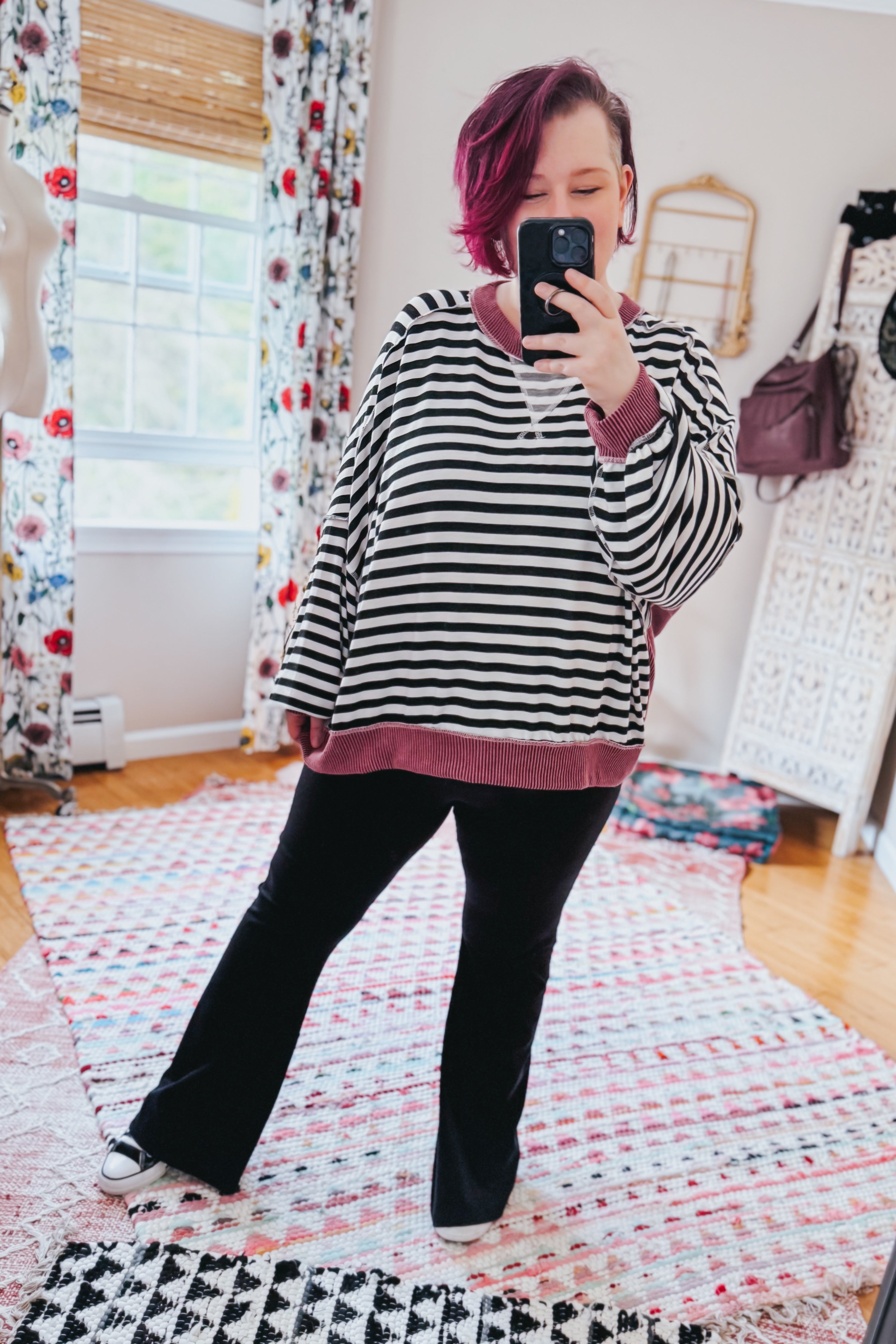 Woman taking selfie wearing black and white striped crew neck pullover with wine ribbed trim and black pants indoors