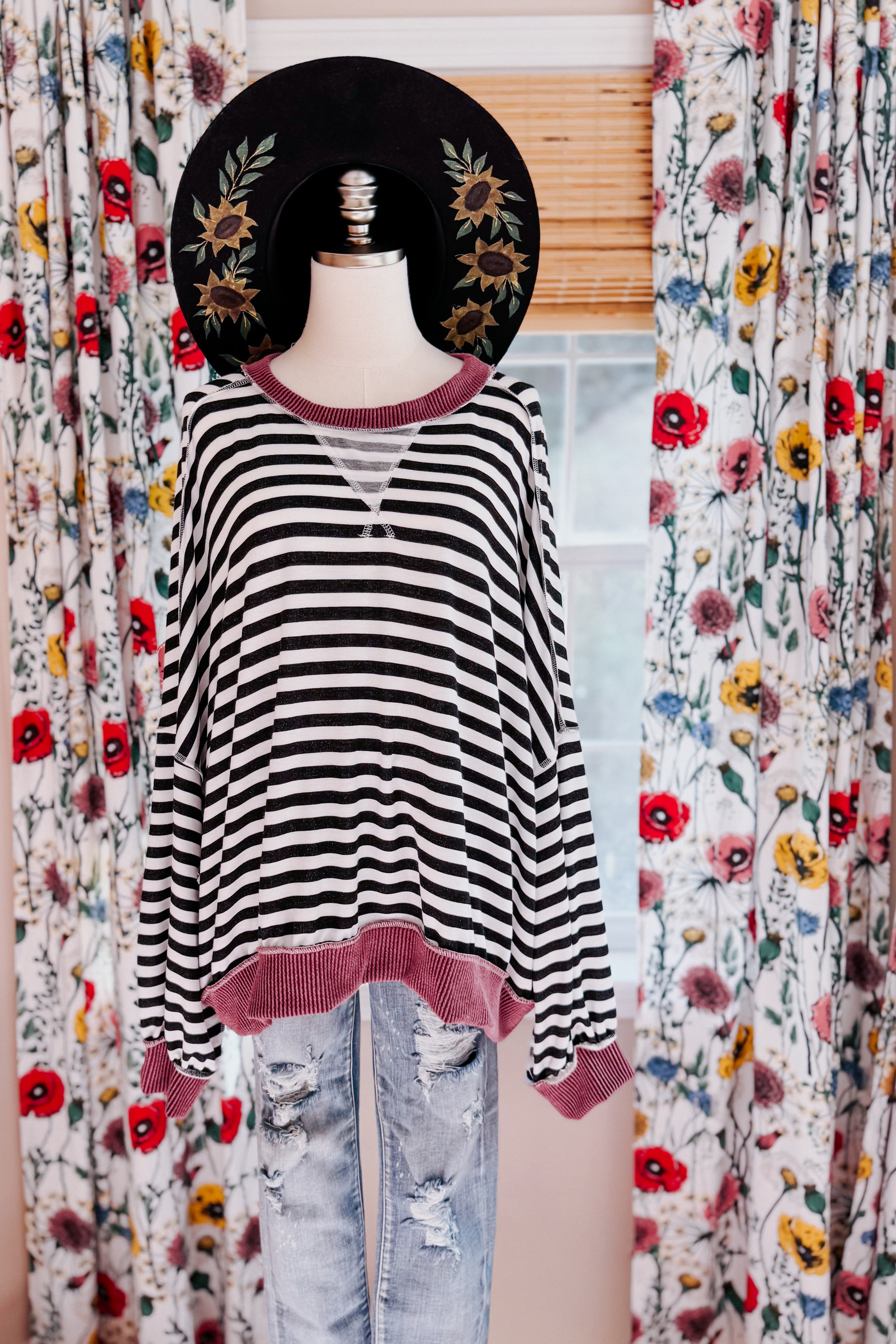 Black and white striped crew neck pullover with wine ribbed cuffs and hem displayed on mannequin with floral hat indoors