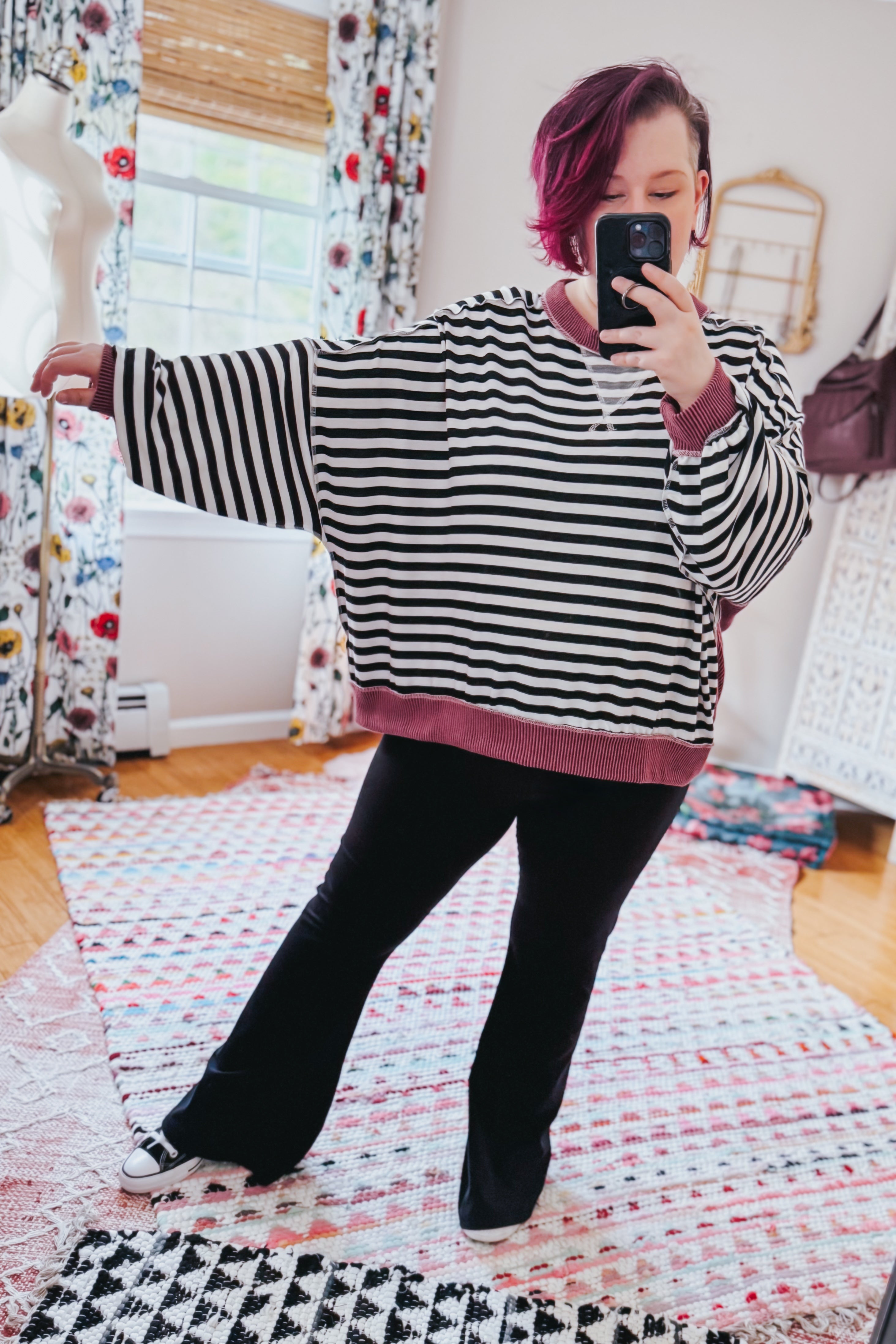 Woman in oversized black and white striped pullover with wine ribbed trim and flared black pants taking selfie indoors