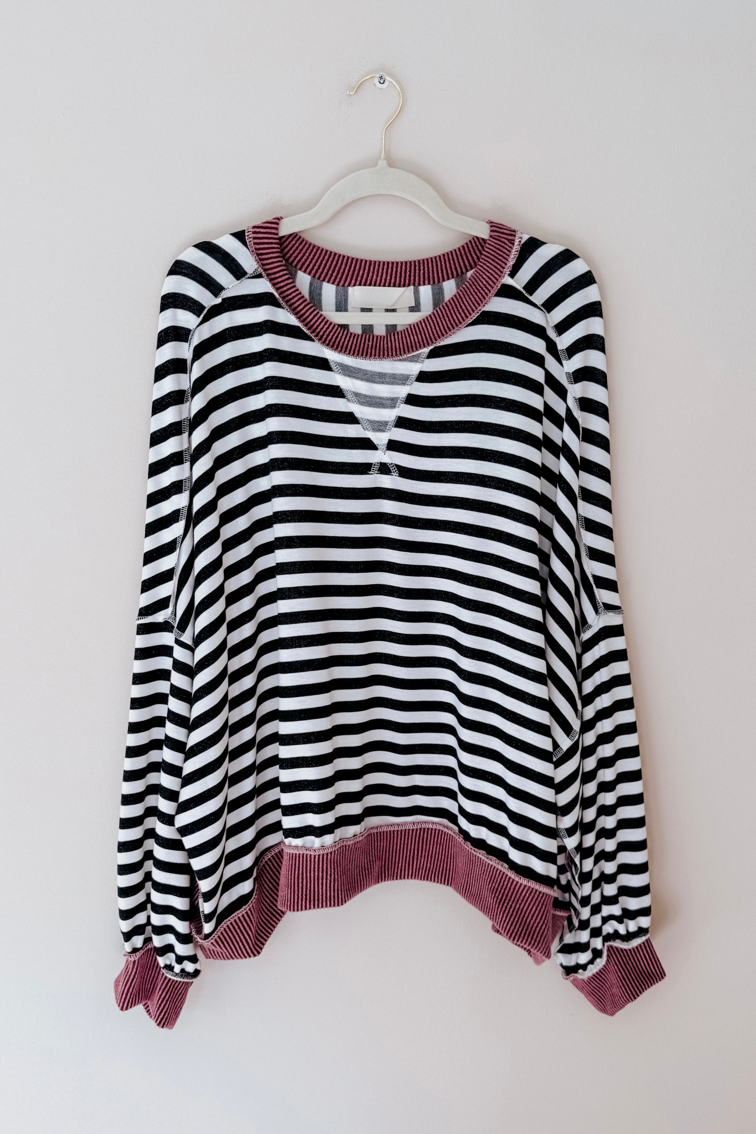 Black and white striped crew neck pullover with textured wine ribbed cuffs, hem, and collar hanging on white hanger against plain wall