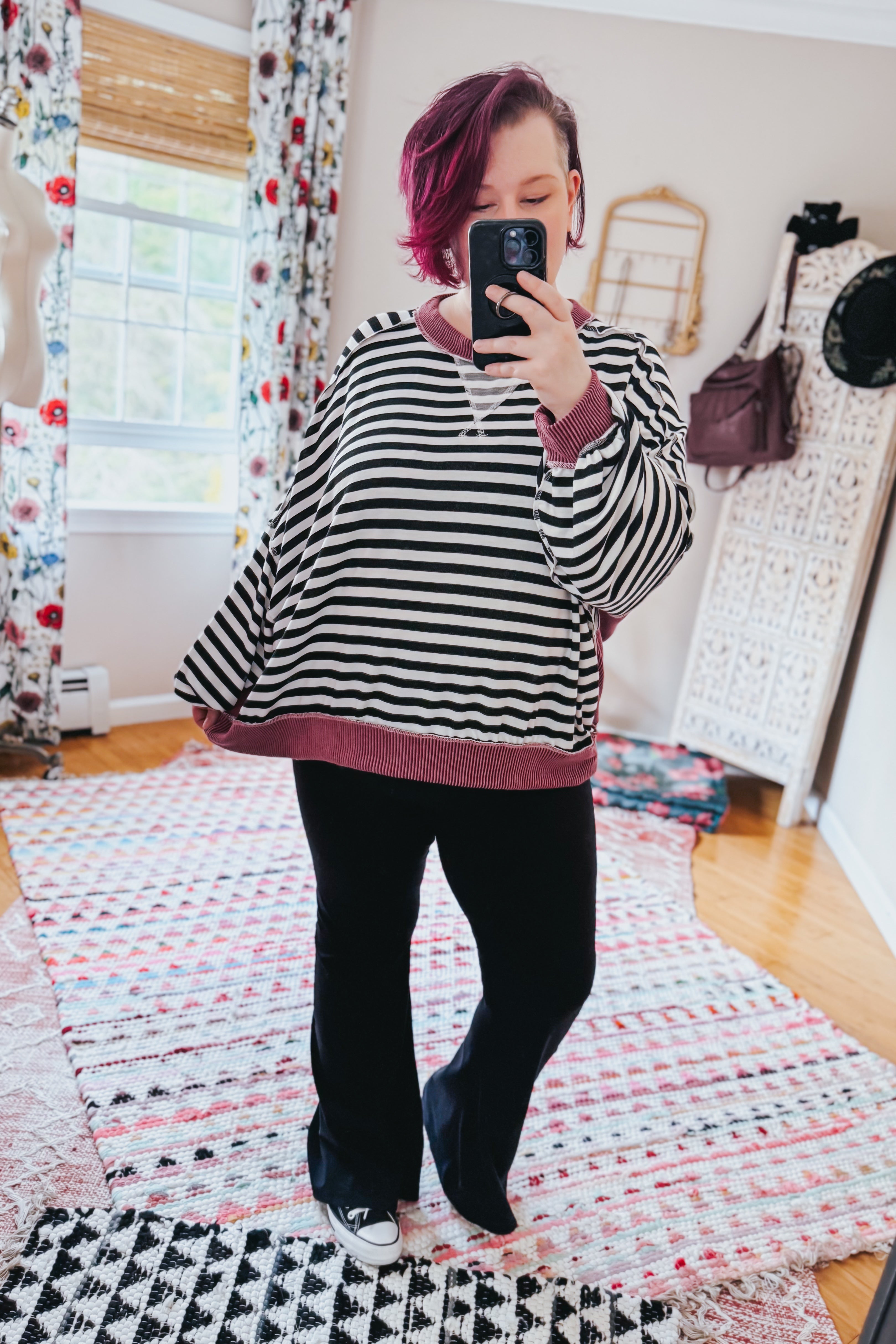Woman with short purple hair wearing loose black and white striped pullover with wine ribbed trim taking mirror selfie indoors