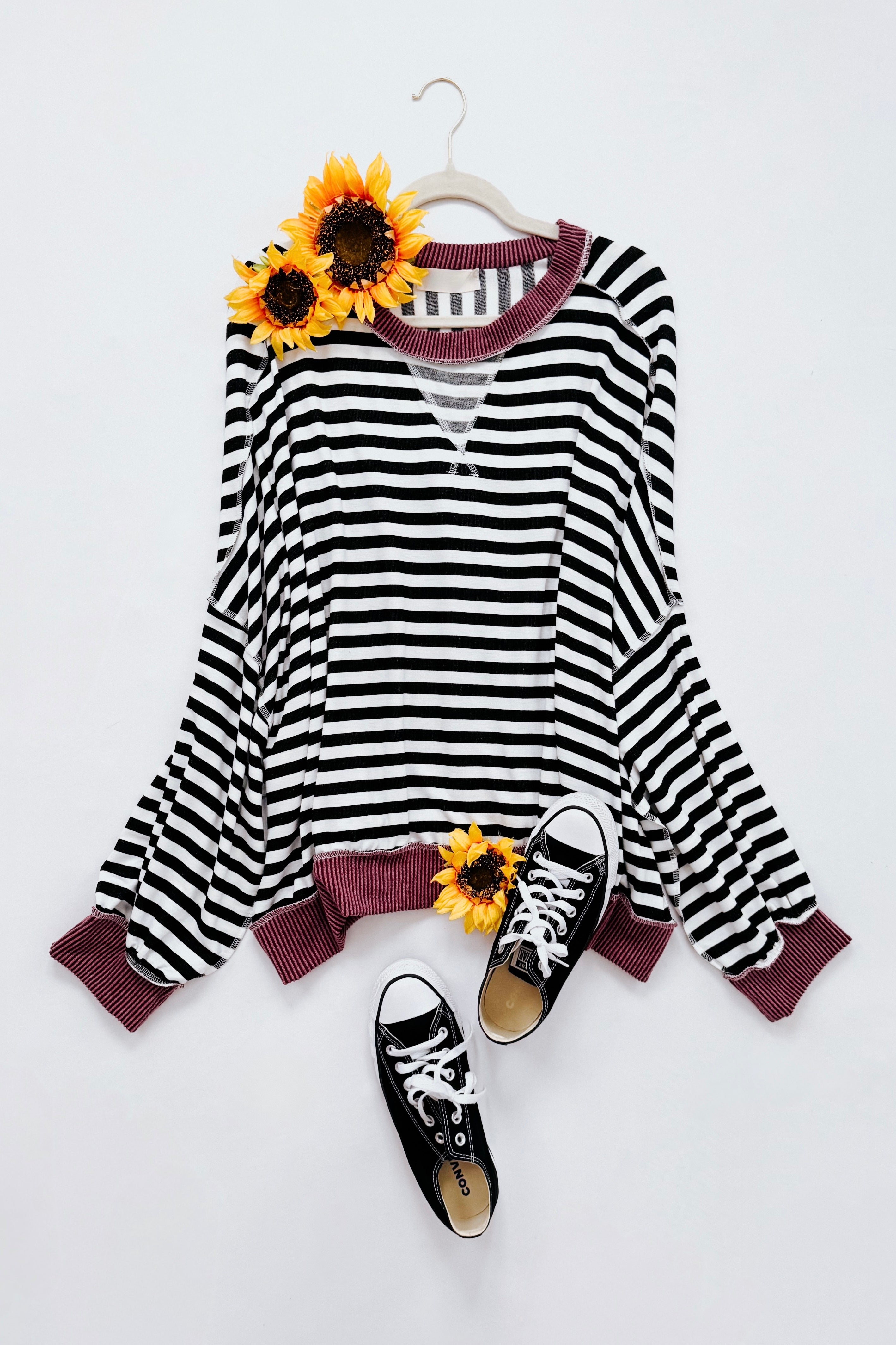 Black and white striped crew neck pullover with wine-colored ribbed collar and hem styled flat with sunflowers and black sneakers