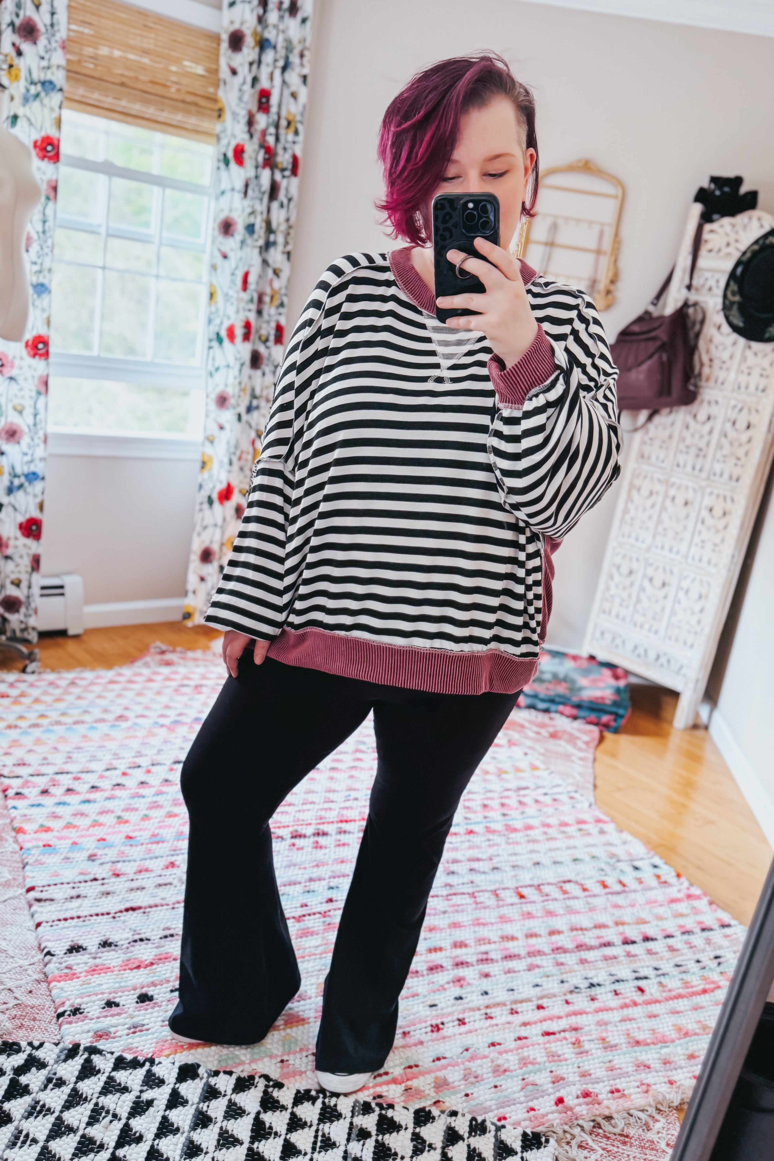 Woman taking mirror selfie wearing black and white striped pullover with wine-colored ribbed trim and black pants indoors