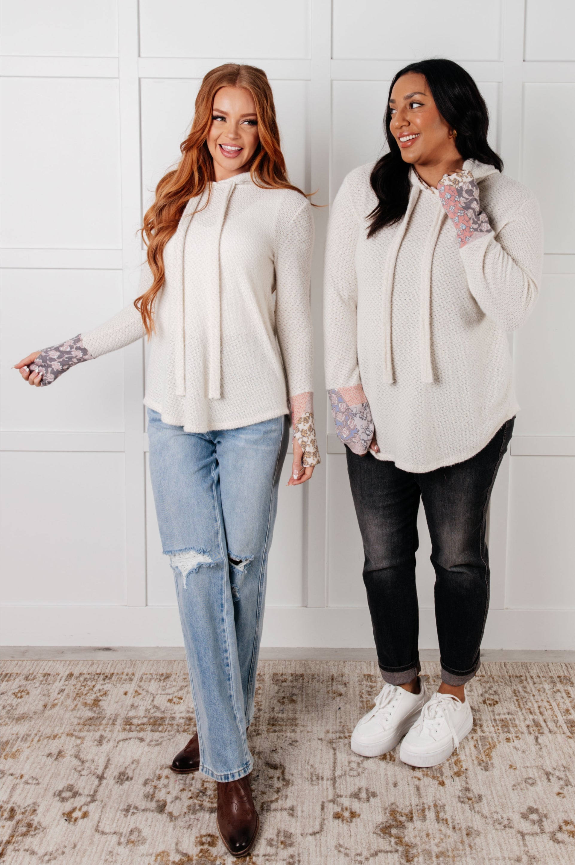 Two Women wearing cream waffle knit hoodies with floral cuffs in an indoor setting.