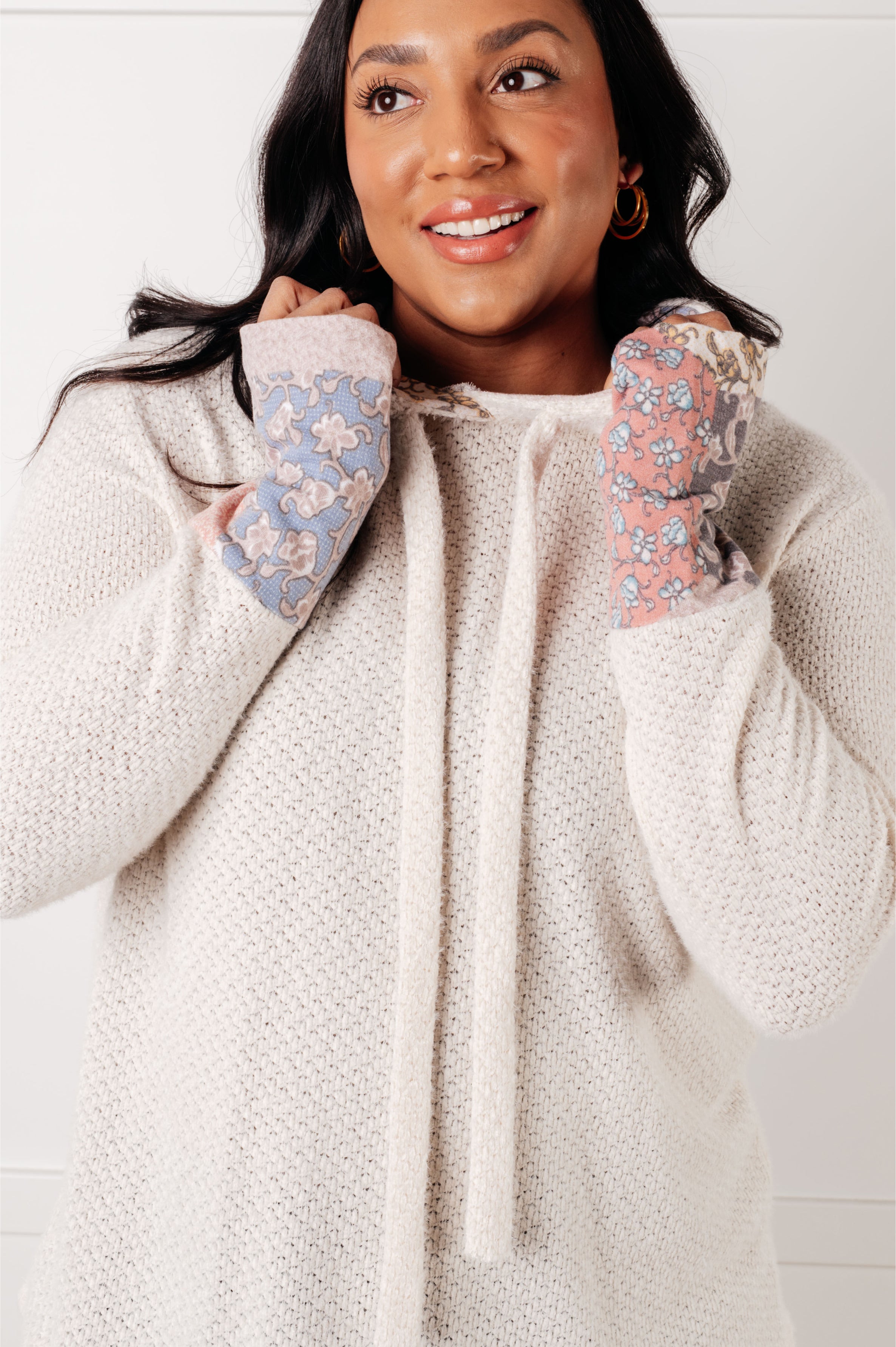 Woman wearing a cream waffle knit hoodie with floral cuffs in an indoor setting.