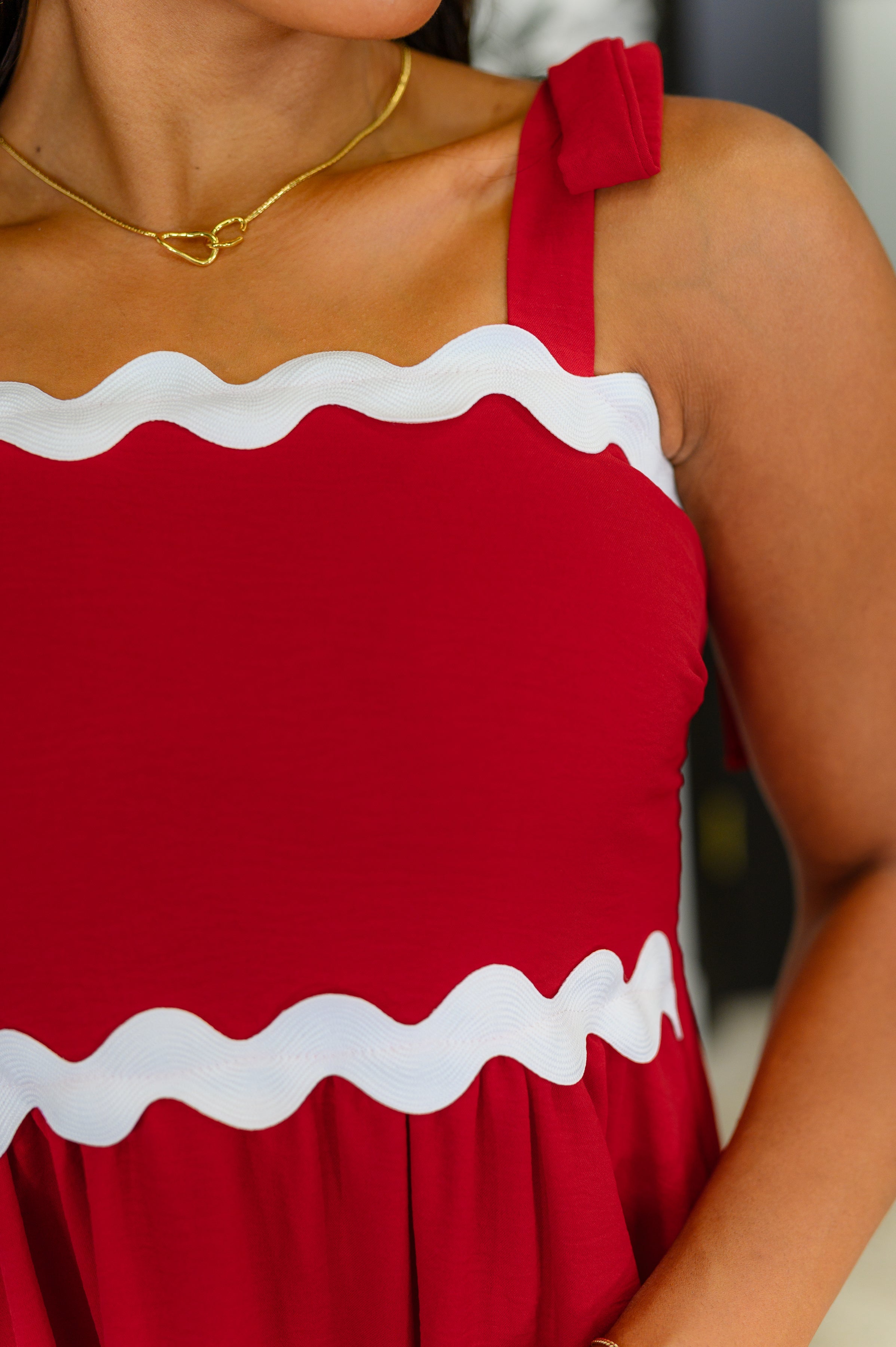 Close-up of red crinkle woven dress with white wavy trim and knotted shoulder strap on model’s upper torso