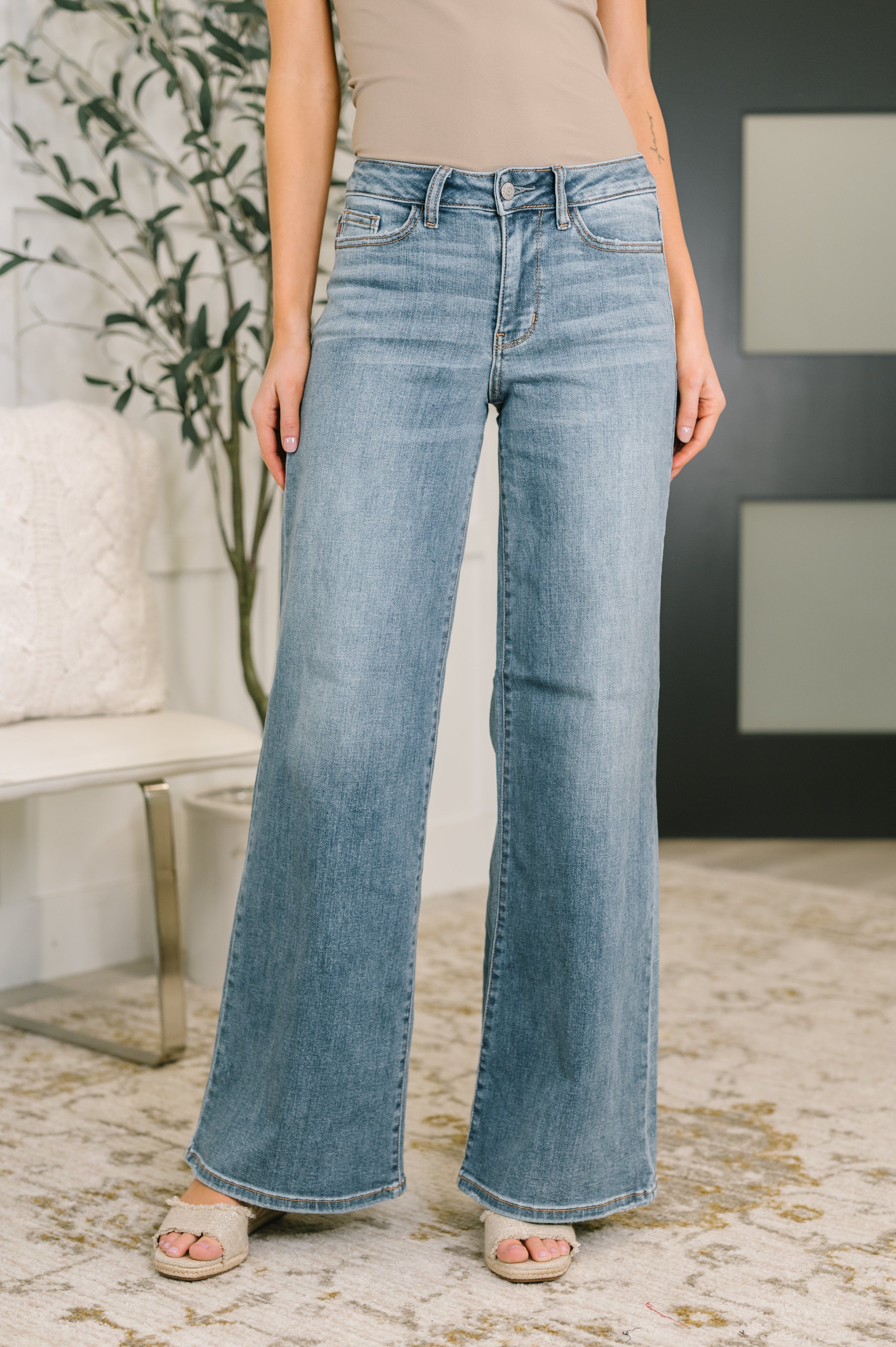 Front view of Adrian mid rise retro wide leg jeans in light blue denim styled with beige top and sandals indoors
