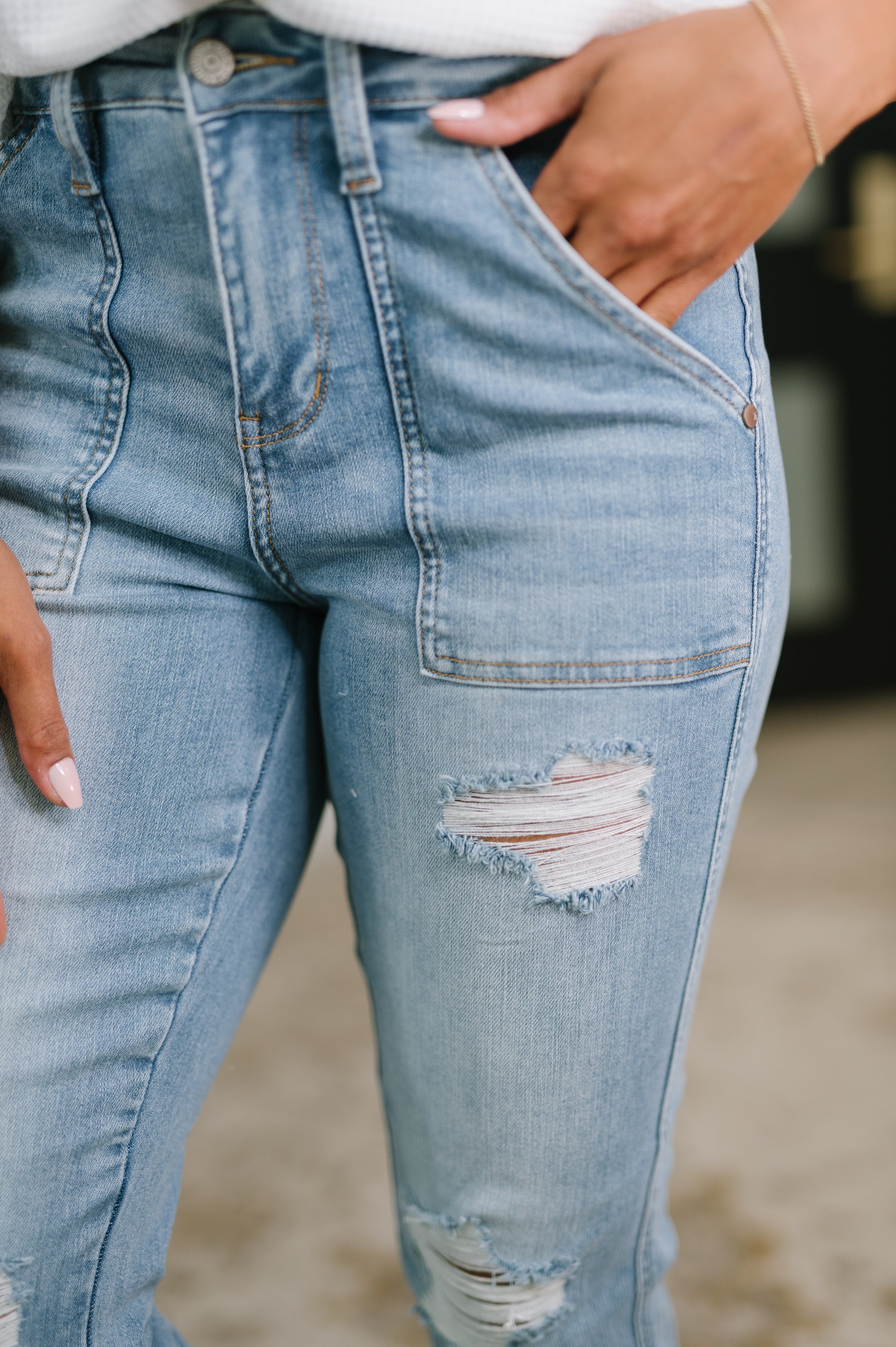 Close-up of distressed light blue high-rise boyfriend jeans with patch pockets worn by a person with a delicate bracelet and manicured nails