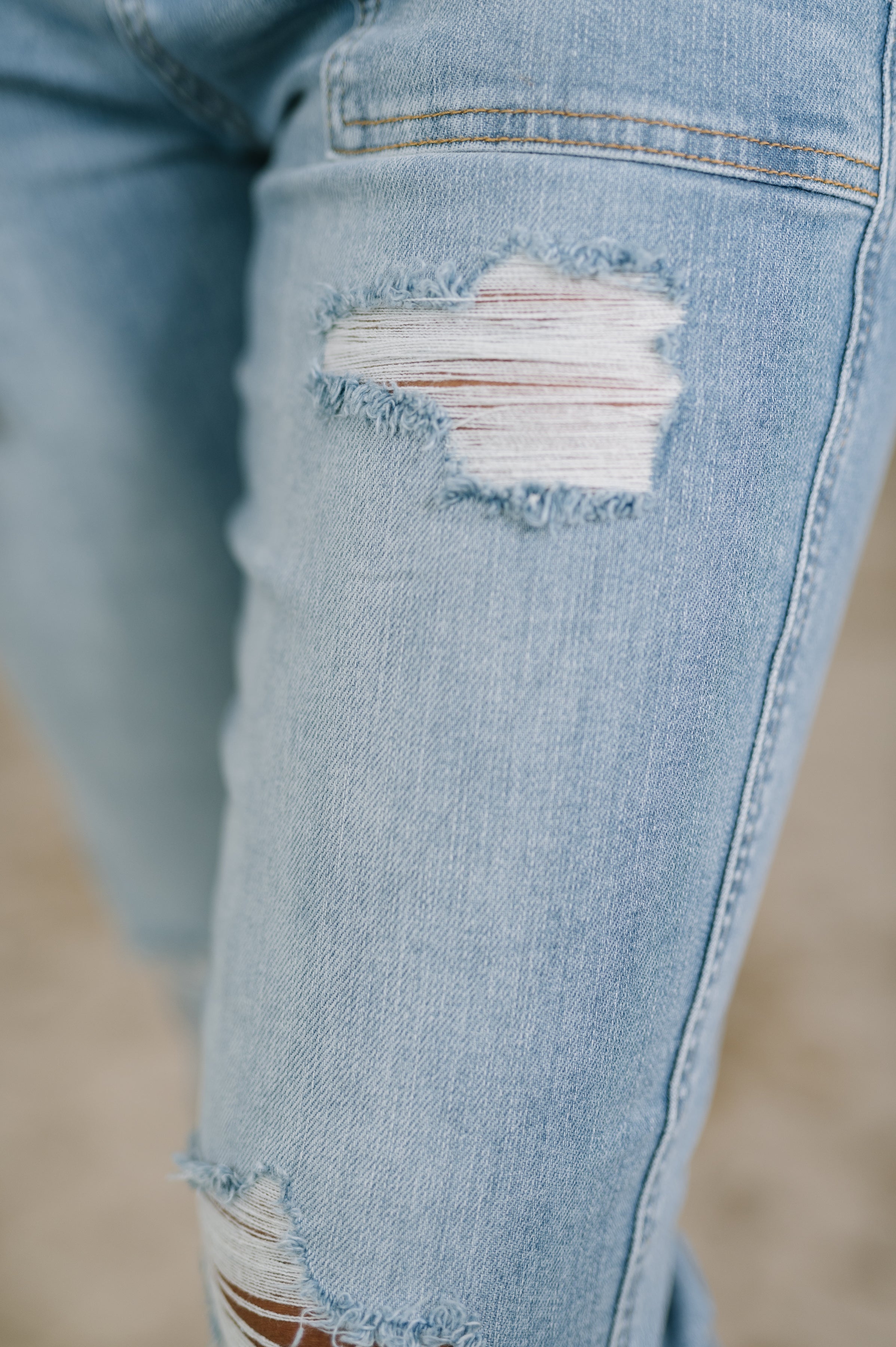 Close-up of light blue distressed jeans with patch pocket and frayed holes on thigh and knee area