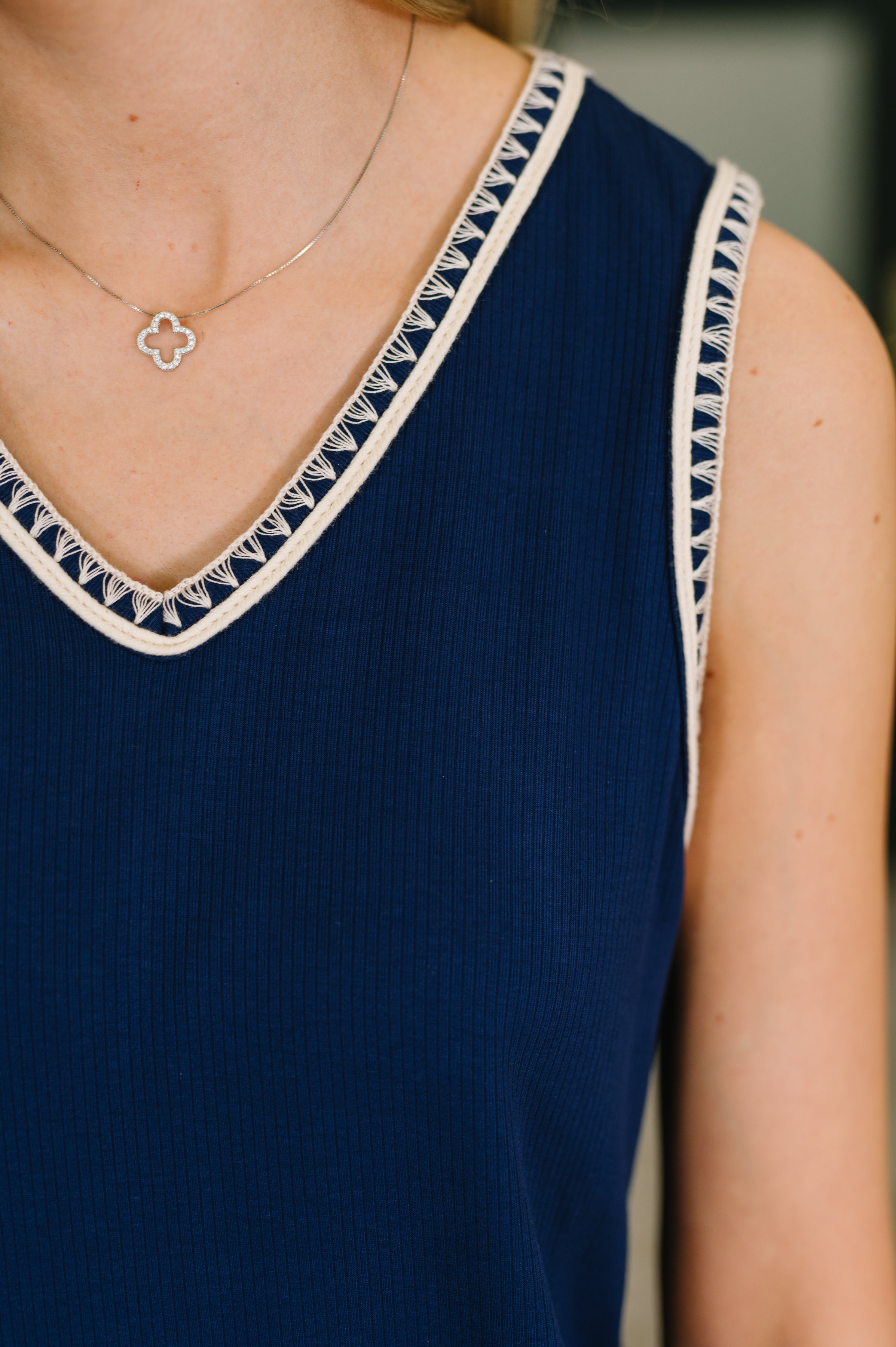 Close-up of navy blue ribbed tank dress with intricate cream trim detail along neckline and armhole worn with delicate necklace