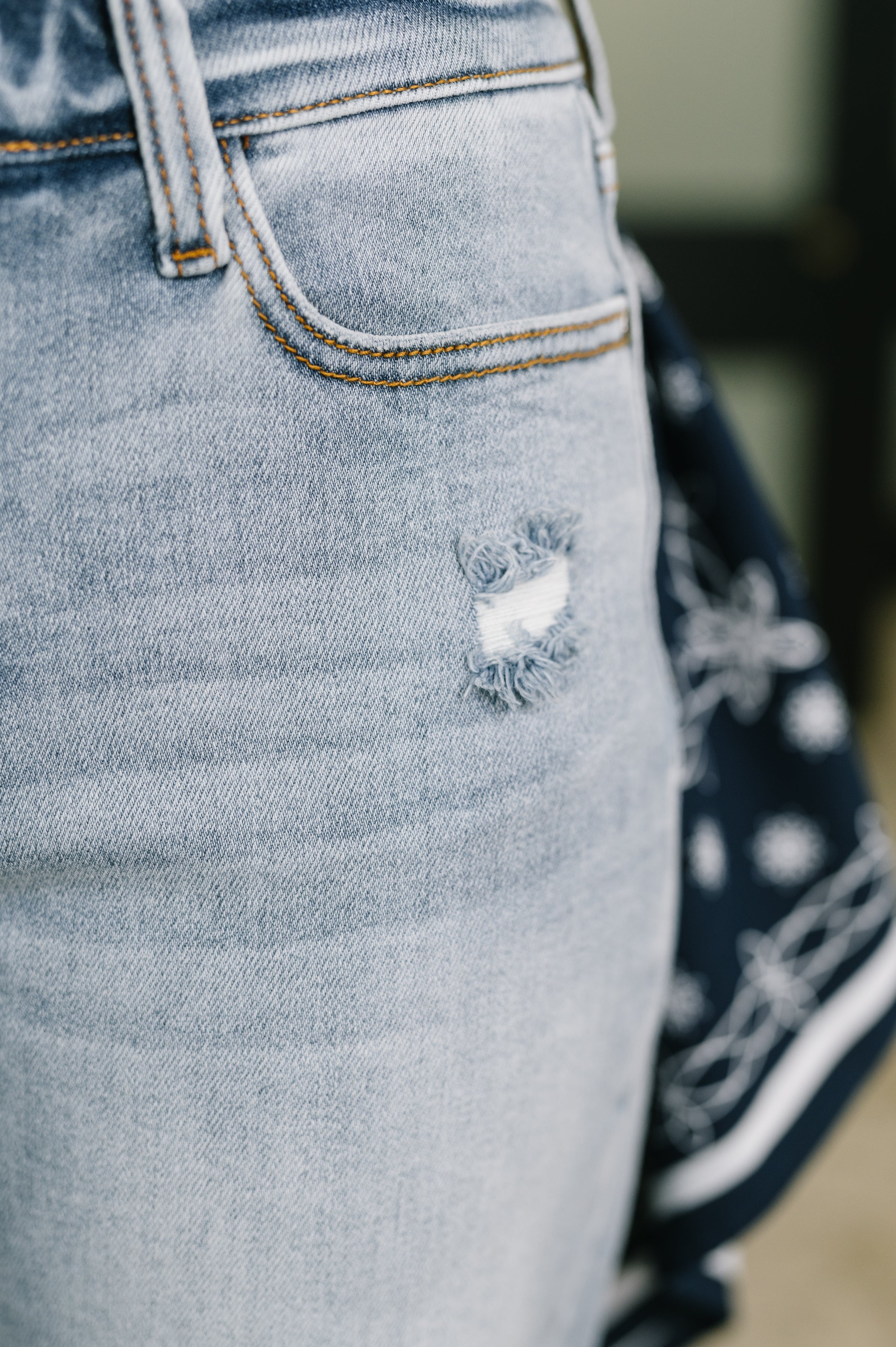 Close-up of light blue mid rise boyfriend jeans with distressed detail and bandana loop accessory visible on the side