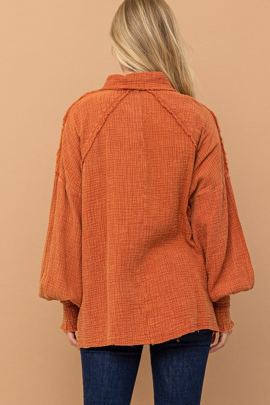 Back view of woman wearing textured burnt orange All Pan Out Ruffled Button Up Shirt with smocked cuffs and balloon sleeves