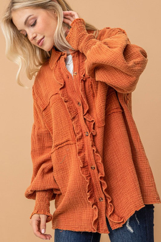Blonde woman wearing oversized textured burnt orange ruffled button-up shirt with smocked cuffs against beige background