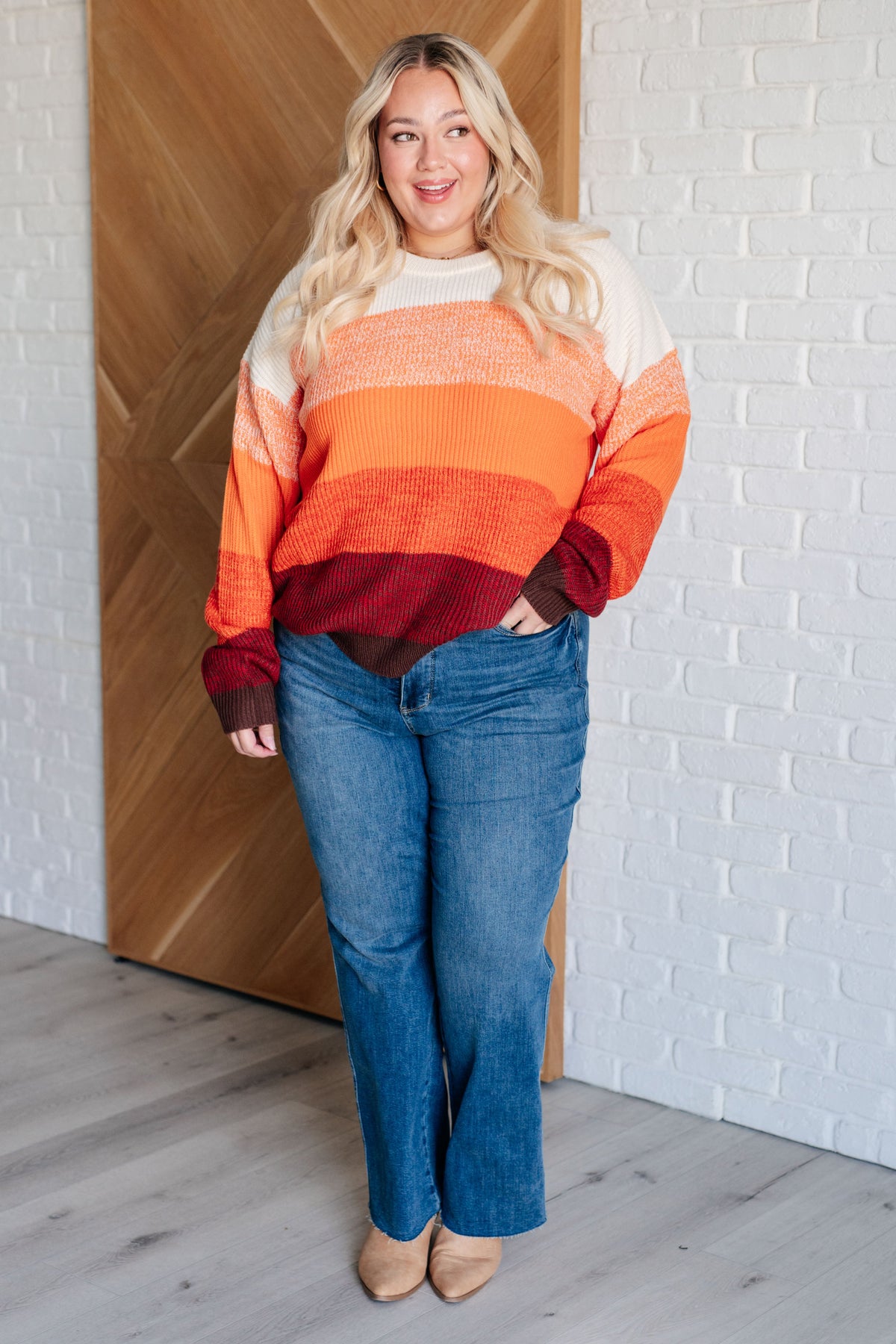 Woman modeling an orange color block sweater with ribbed neckline and cuffs paired with blue jeans indoors