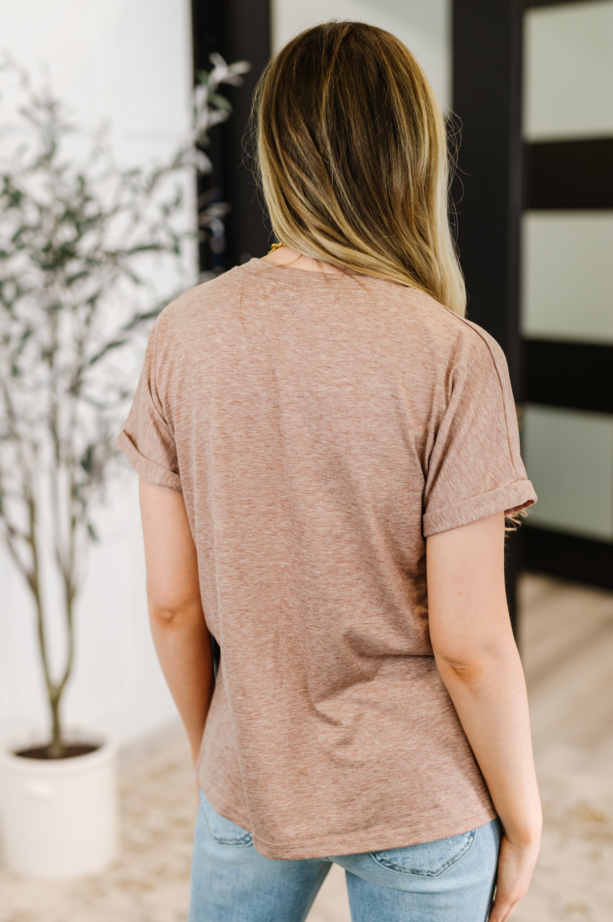 Back view of woman wearing taupe Almost There V-Neck Henley Top with rolled sleeves indoors
