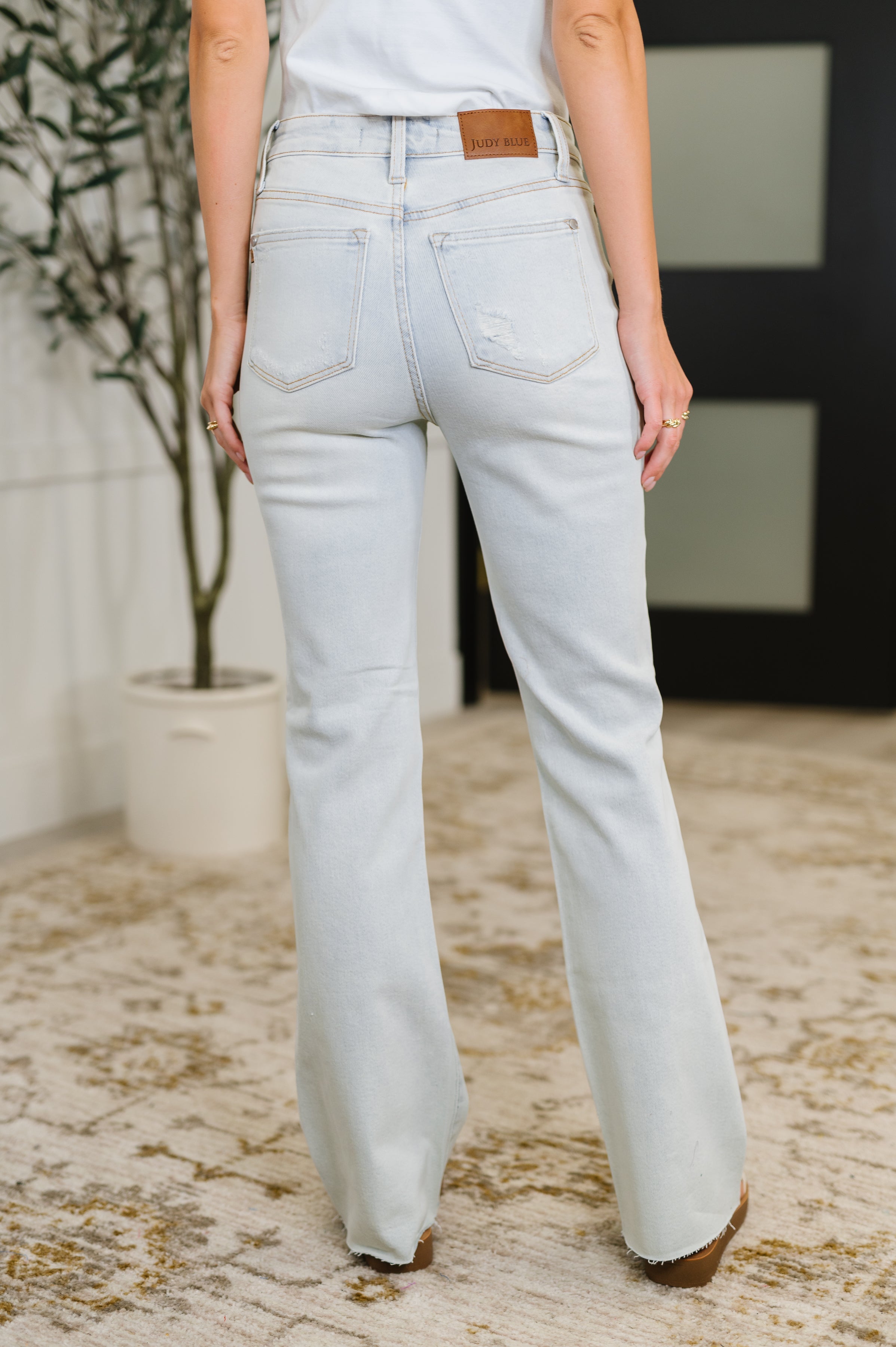 Back view of woman wearing light wash Alyse Mid Rise Destroy & Fray Hem Bootcut jeans indoors Alyse-9.jpg